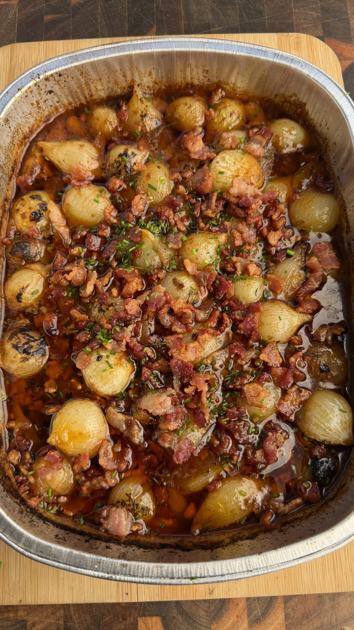 Mini Cajun onion boil with crispy bacon pieces and herbs in aluminum baking pan on wooden cutting board