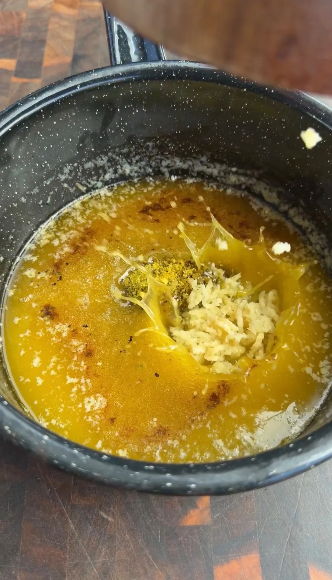 Mini Cajun onion boil simmering in golden broth with spices in a speckled black pot