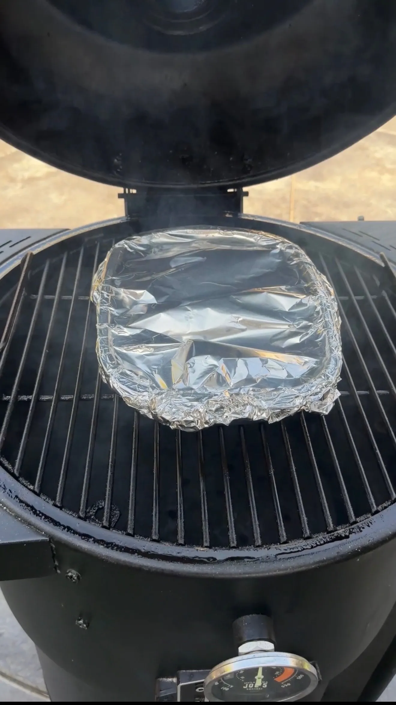 Mini Cajun onion boil wrapped in aluminum foil cooking on a round kettle grill grates