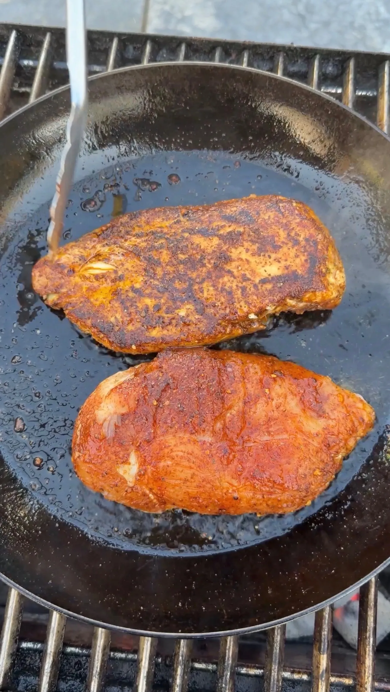Two golden-brown Cajun seasoned chicken breasts searing in a cast iron skillet with oil and spices