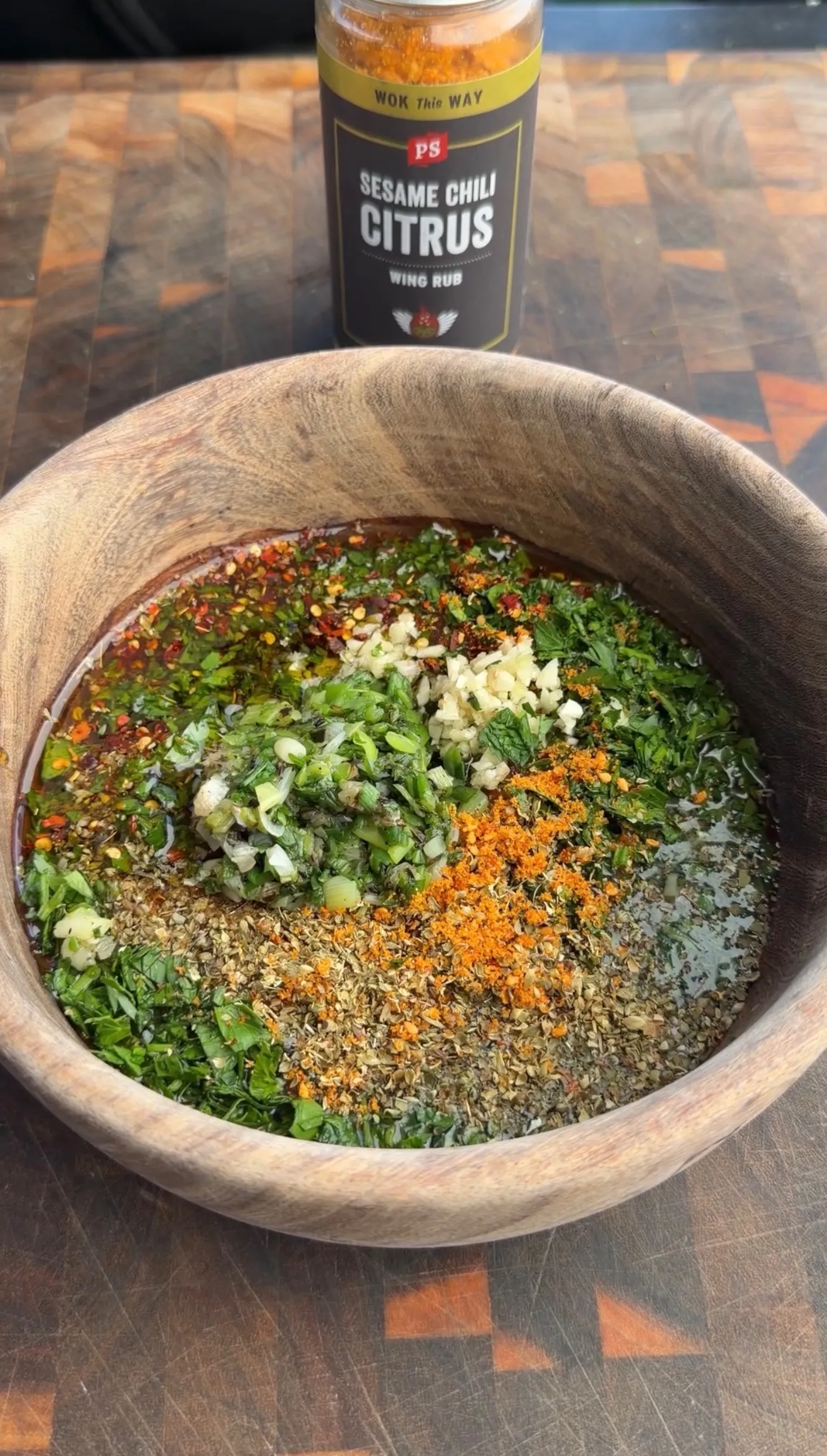 Fresh chimichurri ingredients including chopped green onions, herbs, and spices mixed in a wooden bowl