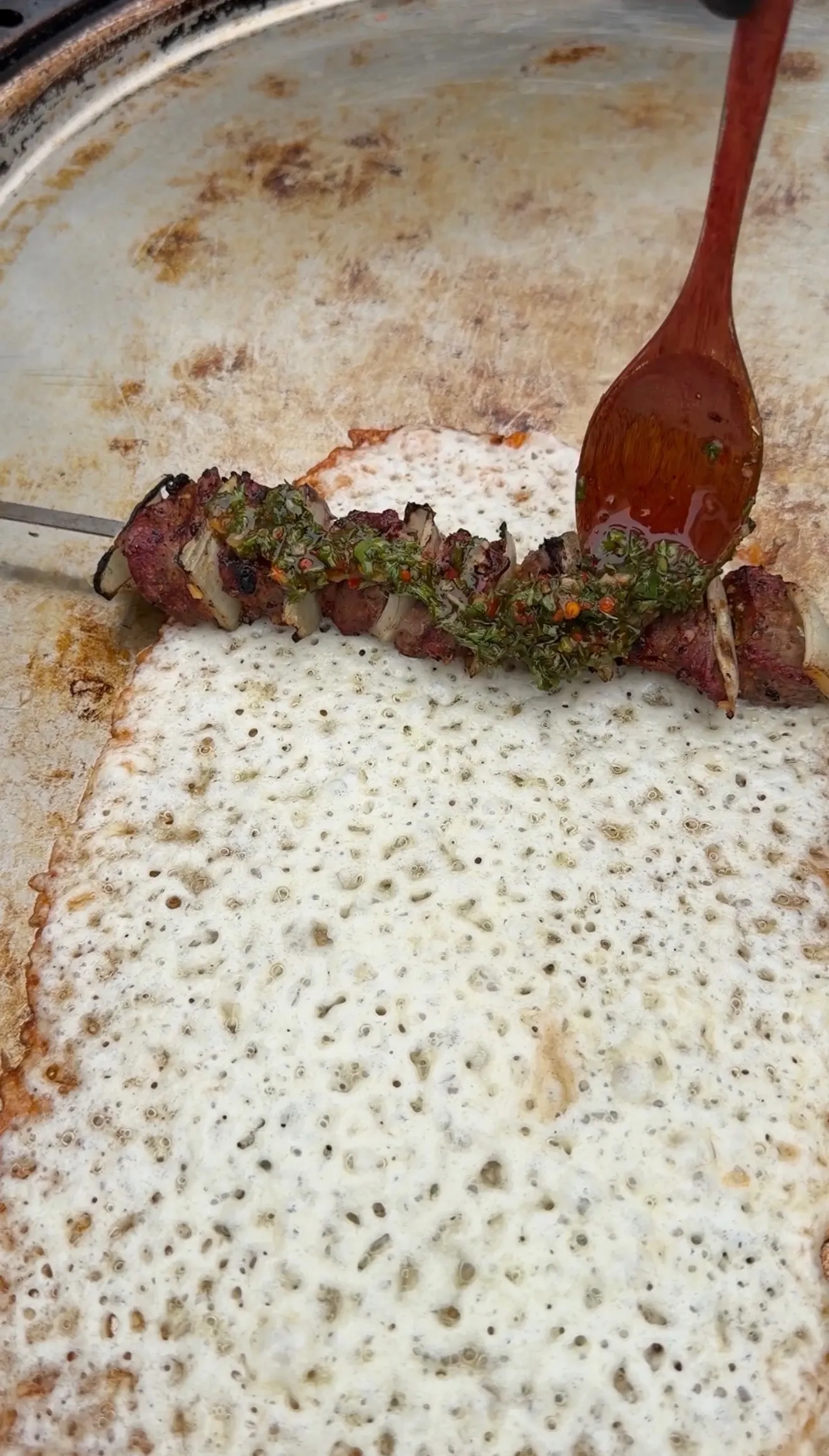 Cheese-crusted steak kebabs with green chimichurri sauce cooking in a bubbly pan with wooden spoon