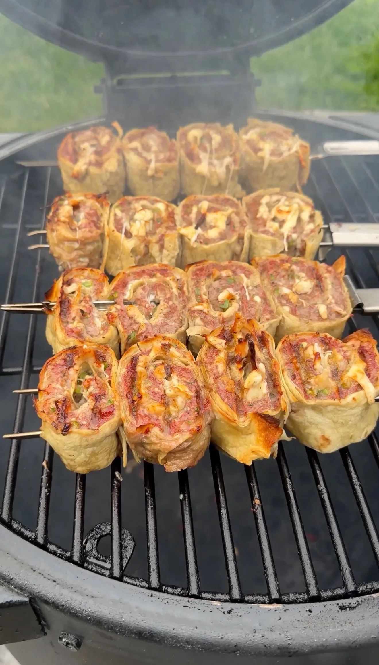 Cheesy beef tortilla pinwheels cooking on a round BBQ grill showing golden-brown spiral patterns