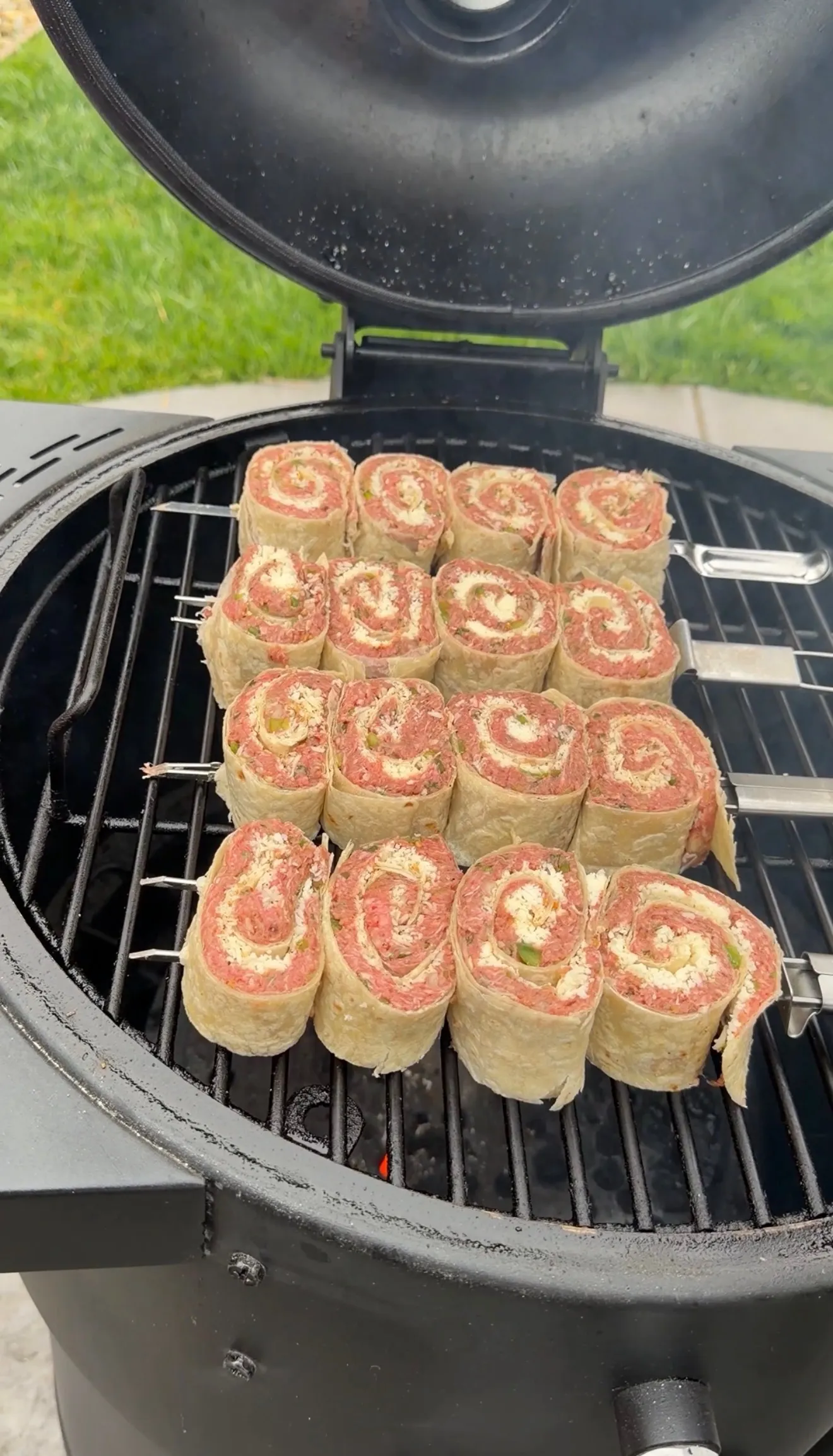 Cheesy beef tortilla pinwheels arranged on a grill grate inside a black kamado-style grill showing spiral pattern