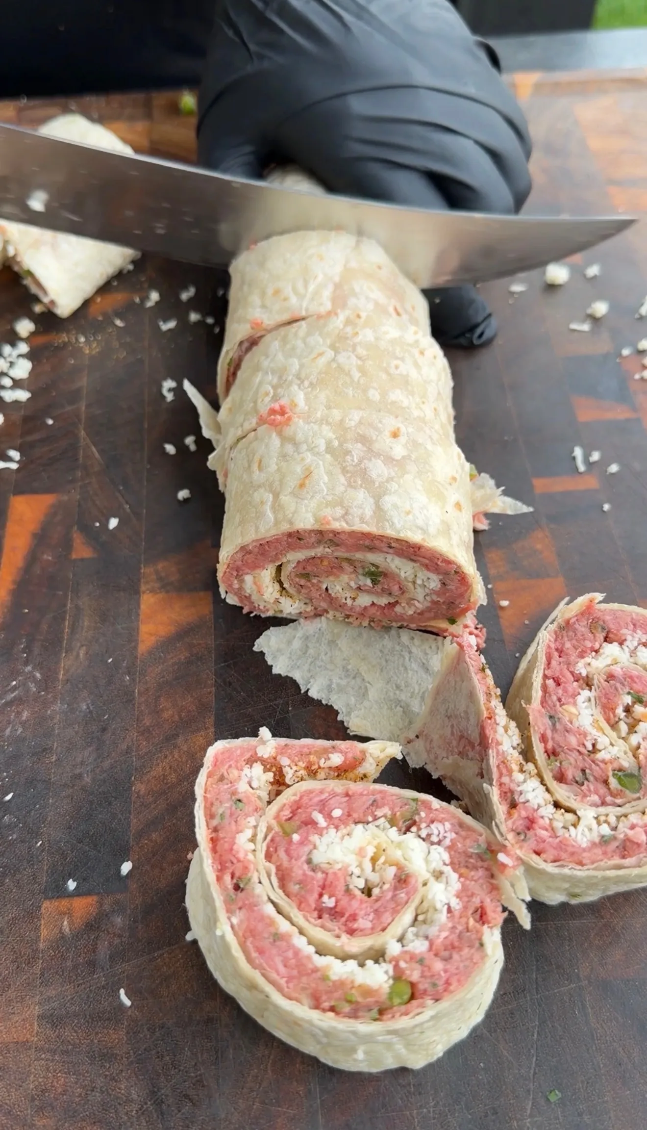 Sliced cheesy beef tortilla pinwheels with spiral filling on a wooden cutting board with chef's knife