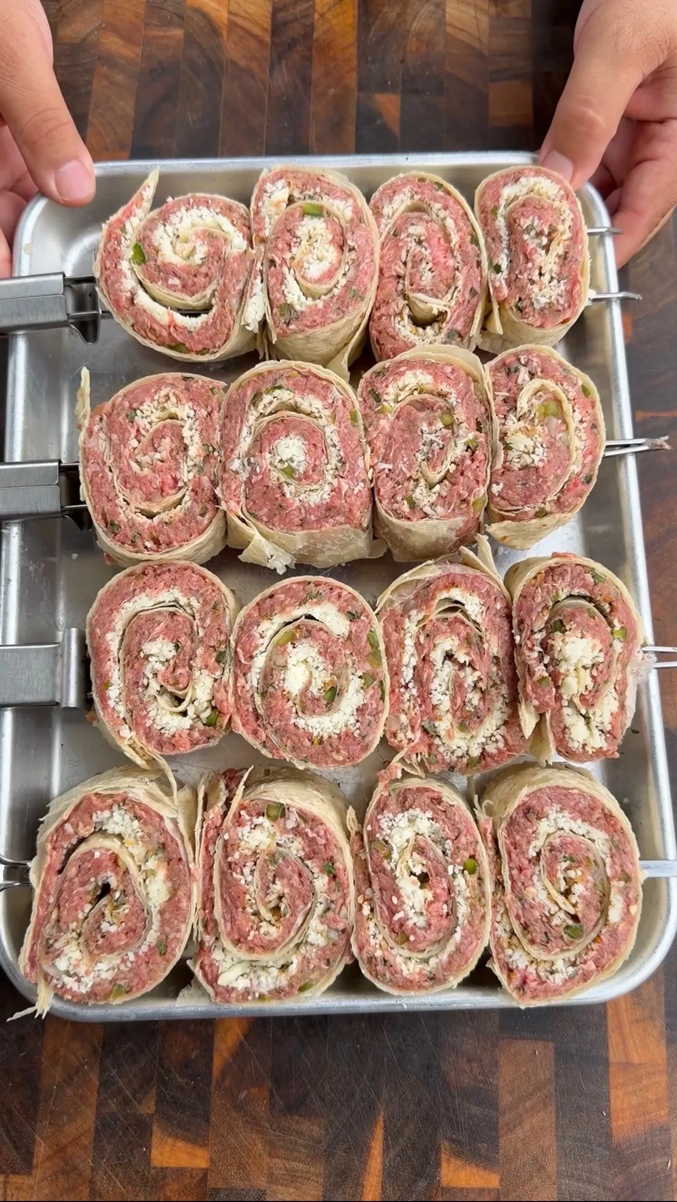 Sliced cheesy beef tortilla pinwheels arranged on metal skewers in a baking pan showing spiral pattern with filling