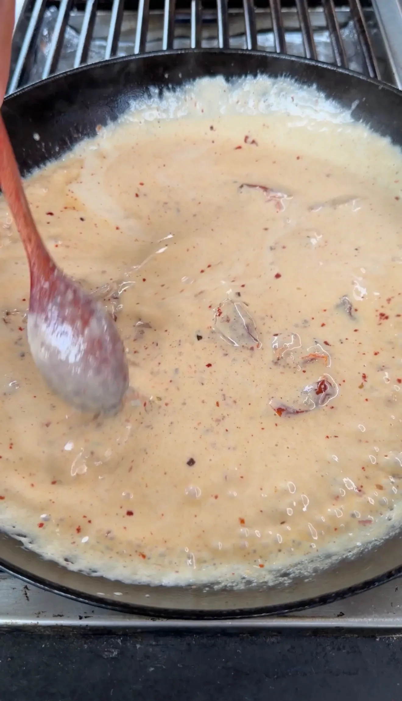 Creamy marry me chicken sauce bubbling in a cast iron skillet with herbs and spices visible