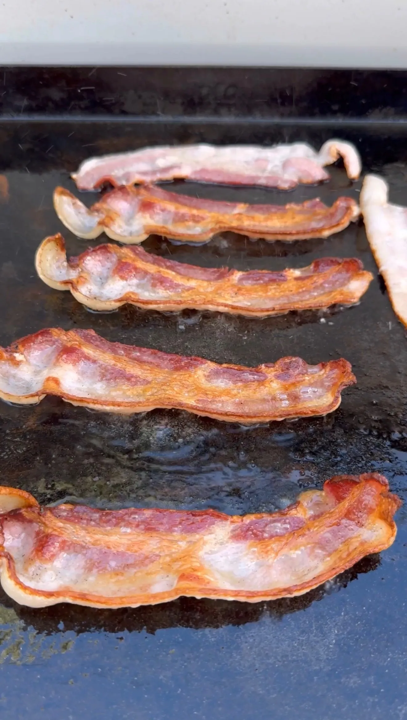 Crispy bacon strips cooking on griddle