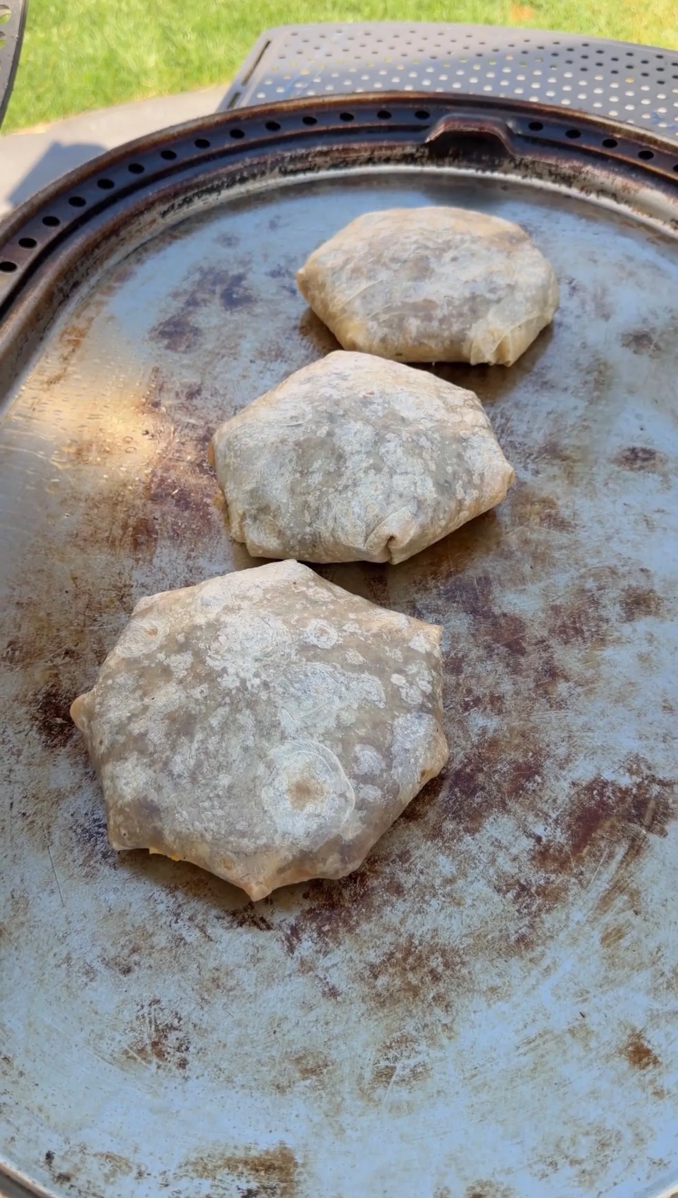 Three classic crunchwraps cooking on a round metal griddle outdoors with golden brown tortilla wraps