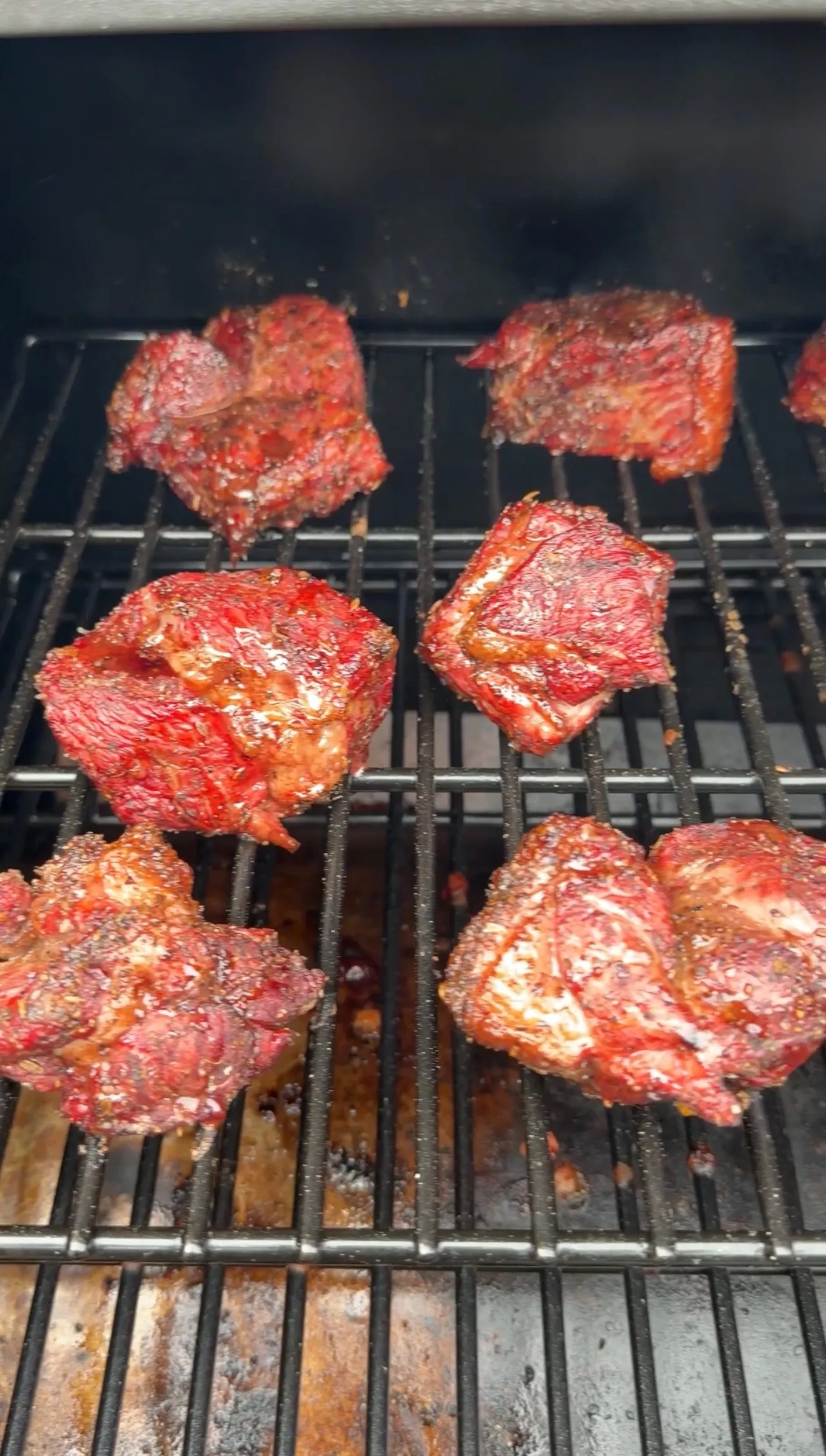 Dr Pepper marinated beef chunks with caramelized glaze smoking on black grill grates over wood coals