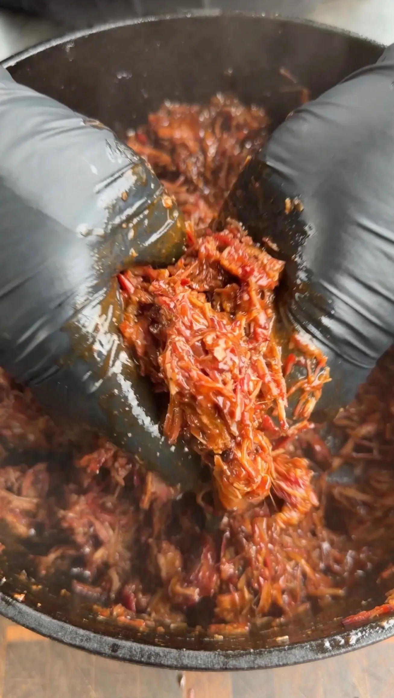 Shredded Dr Pepper pulled beef being lifted from a cooking pot with tongs, showing tender caramelized meat