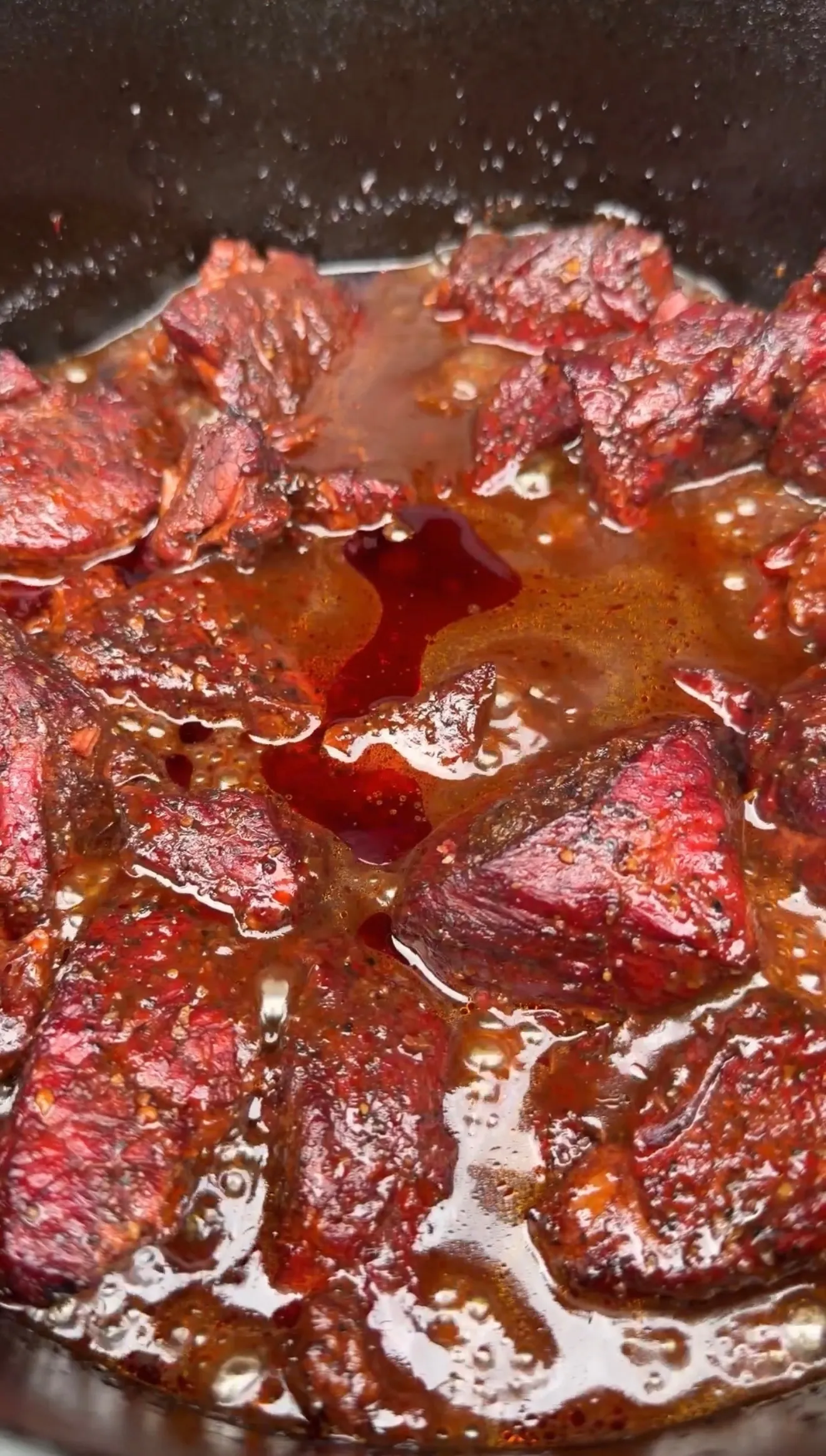 Dr Pepper pulled beef cooking in a pan with rich brown sauce, showing tender shredded meat simmering