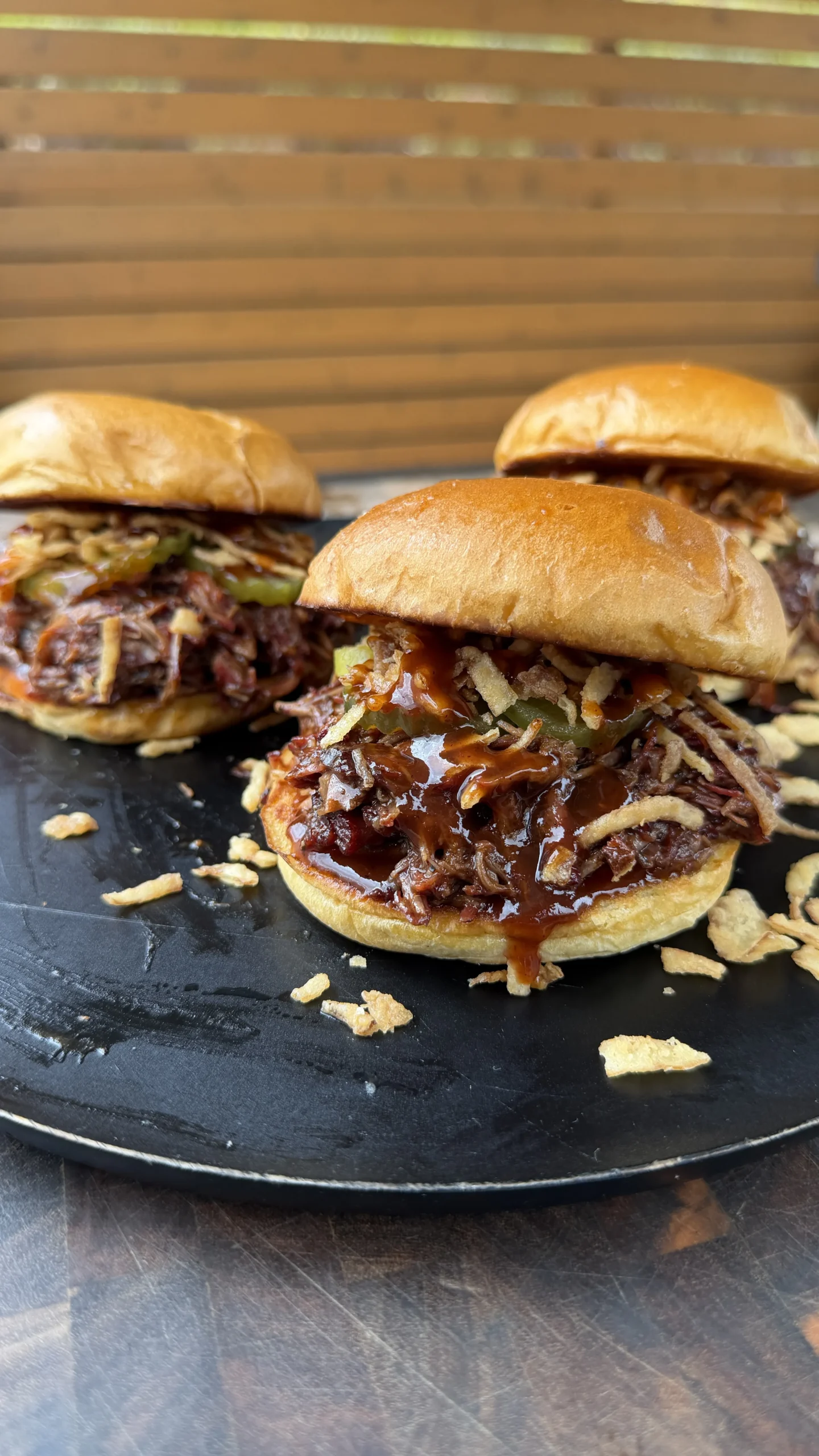 Three Dr Pepper pulled beef sandwiches with caramelized onions and barbecue sauce on golden brioche buns on slate plate