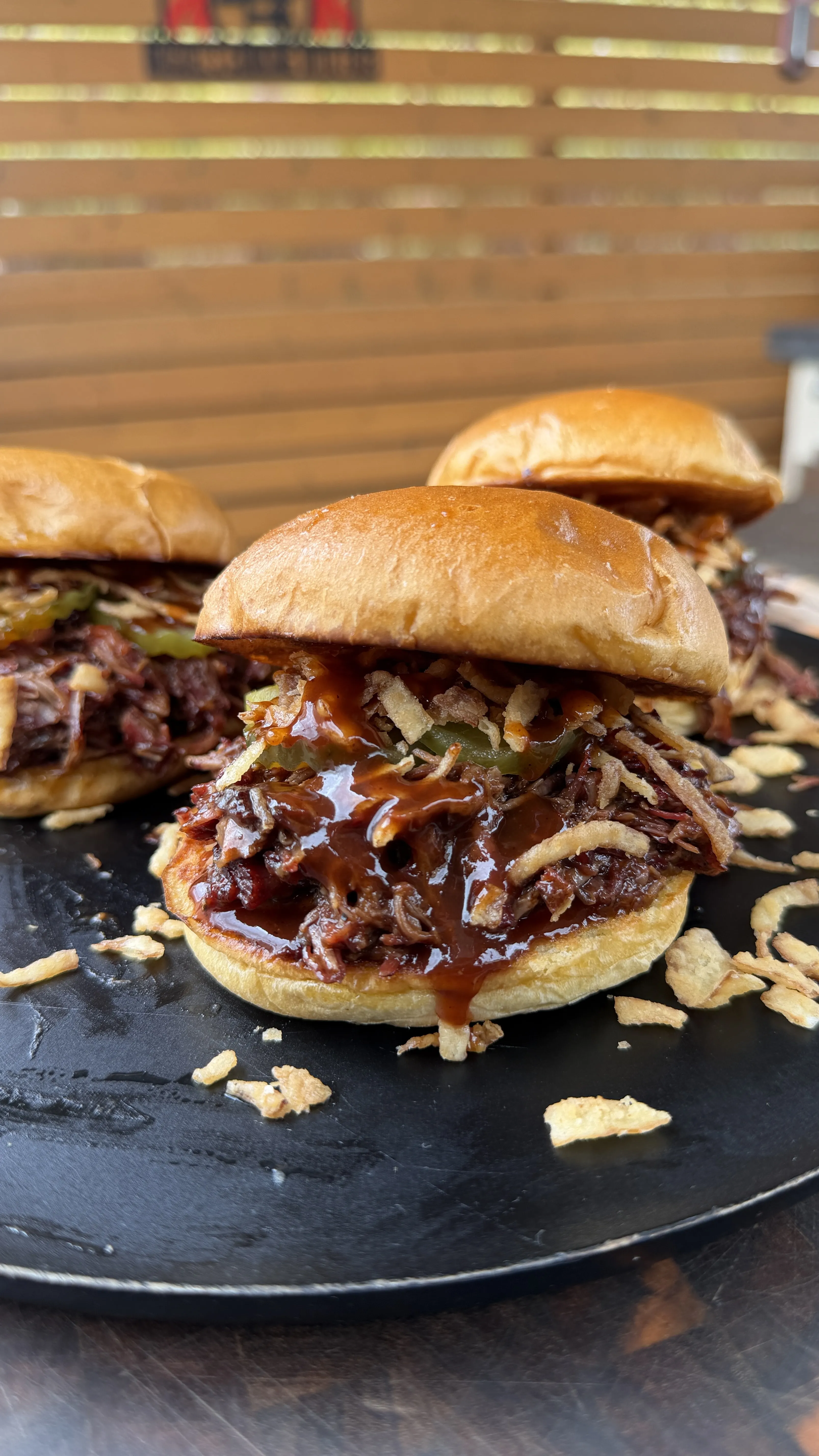Dr Pepper pulled beef sandwiches with barbecue sauce on brioche buns served on a black slate board