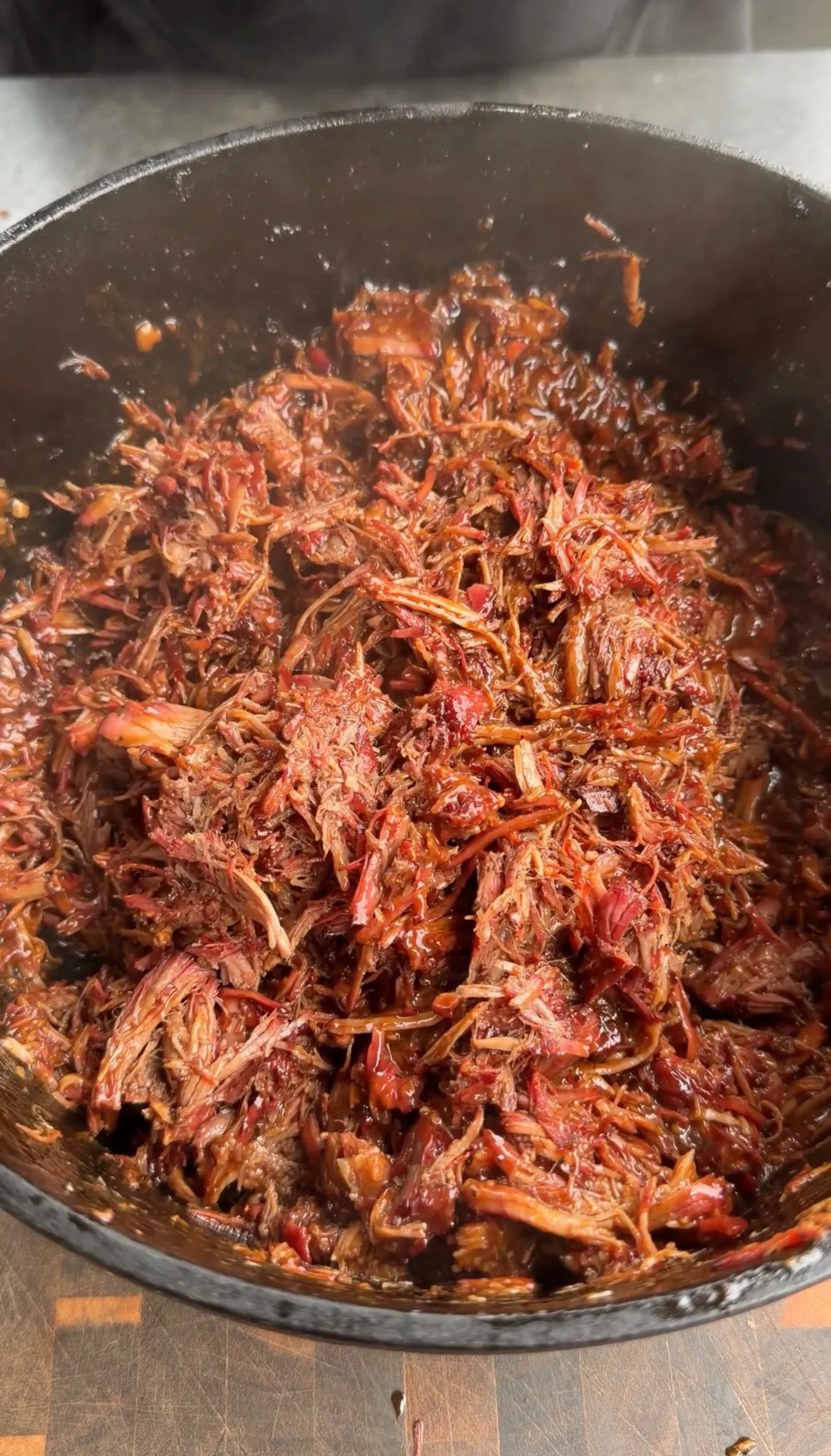 Shredded Dr Pepper pulled beef with rich brown sauce cooking in a dark cast iron skillet