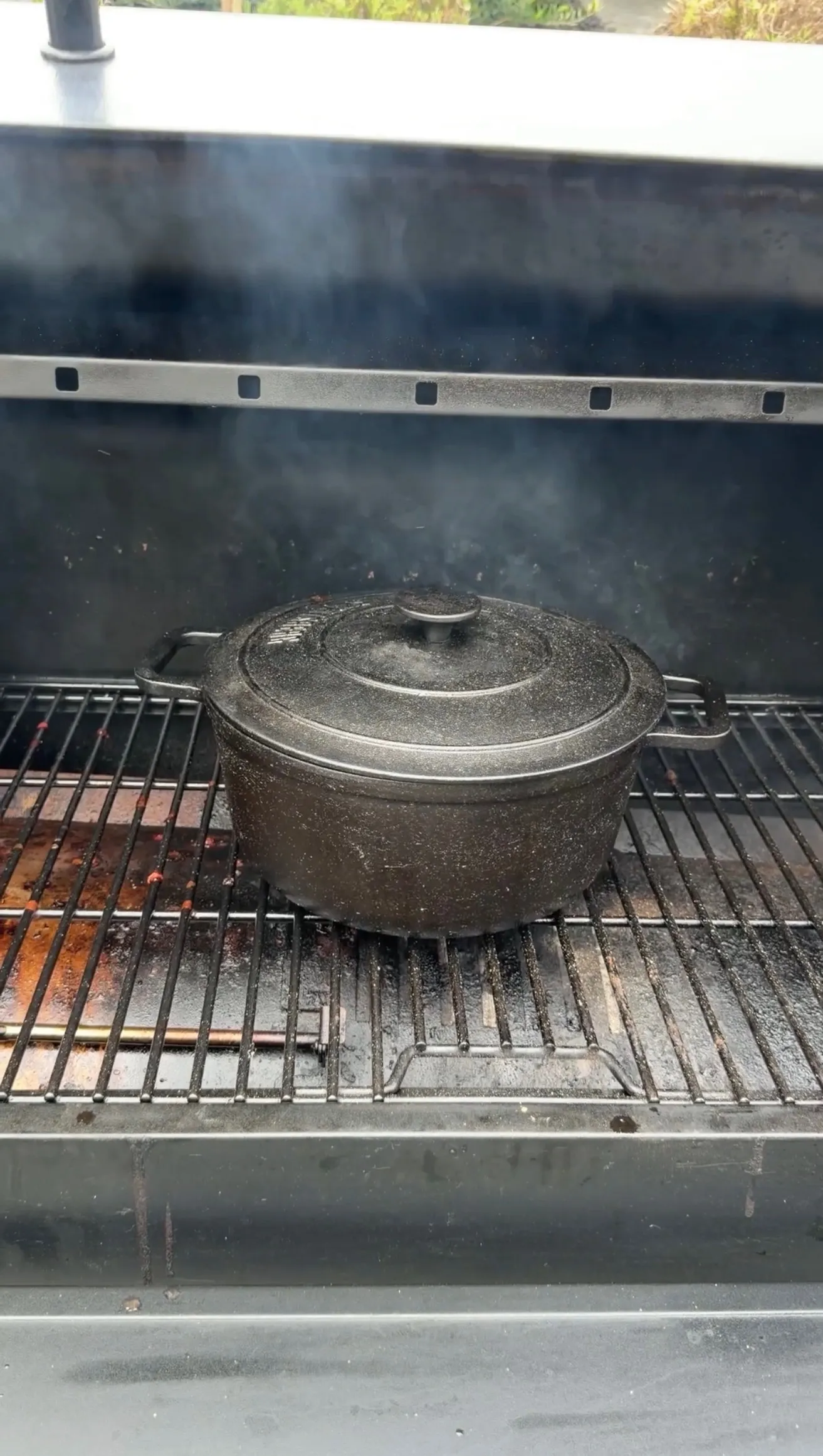 Cast iron Dutch oven with lid cooking Dr Pepper pulled beef on outdoor grill grates