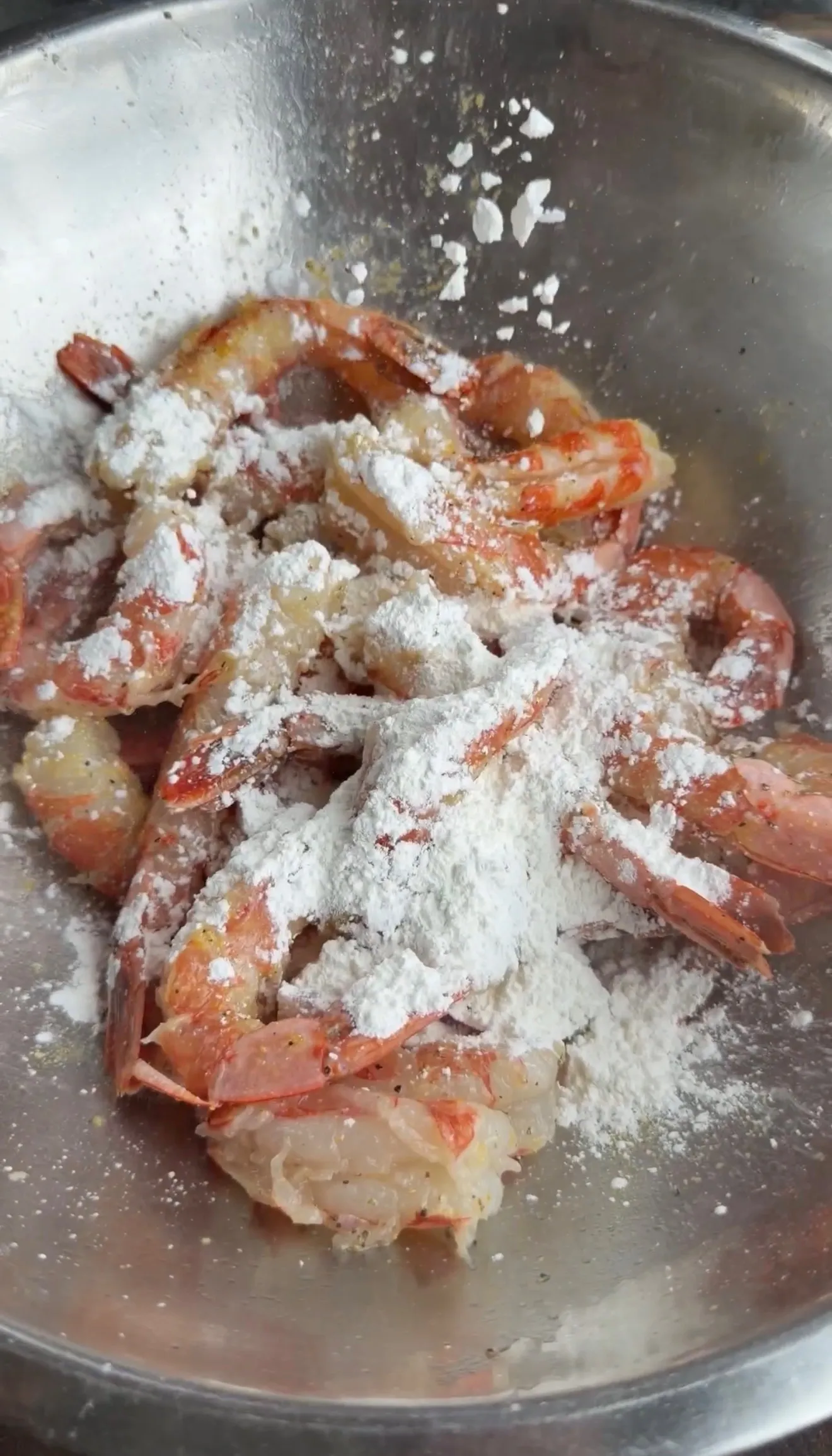 Raw shrimp coated in flour in a metal mixing bowl during preparation for lemon pepper crispy shrimp