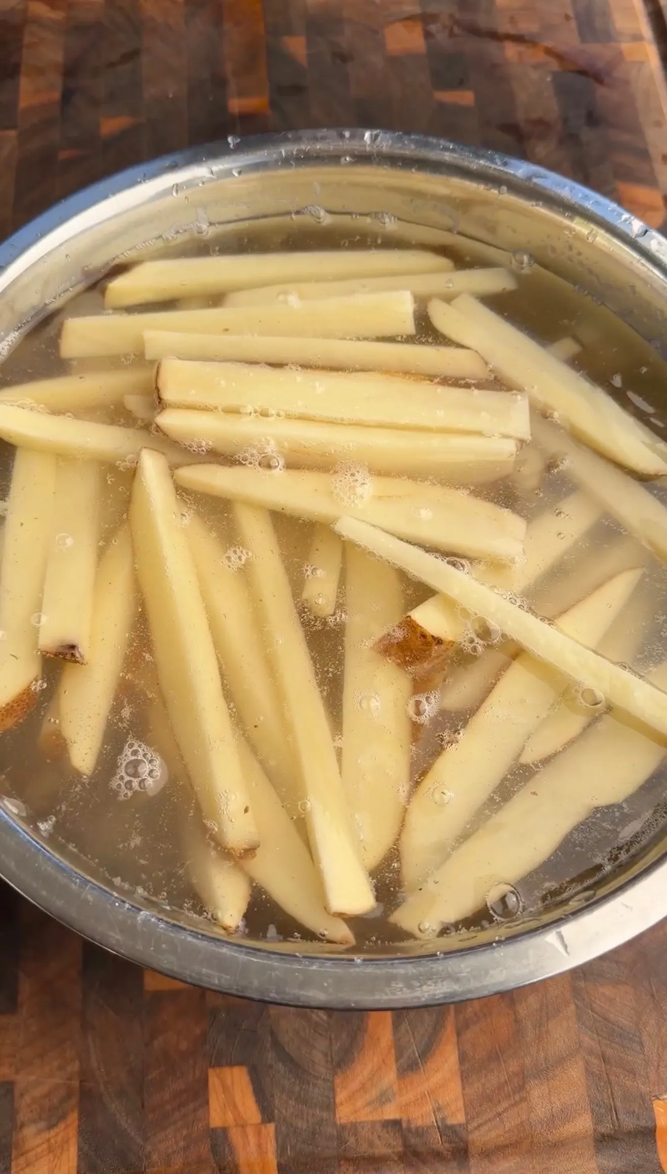 Fresh cut potato fries cooking in boiling water in a metal pot preparing for crispy fries recipe
