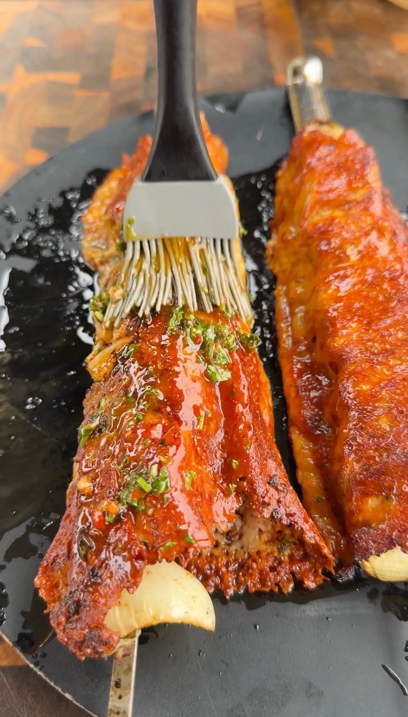 Cheese-crusted chimichurri steak kebabs being basted with sauce in a cast iron pan garnished with herbs