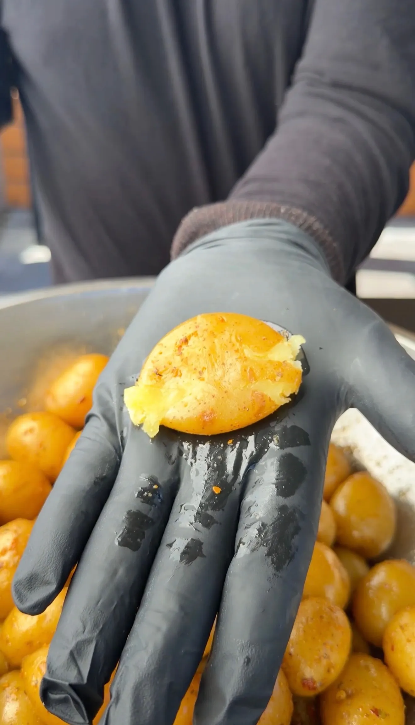 Hand in black glove holding a golden smashed mini potato with crispy edges over pile of roasted potatoes