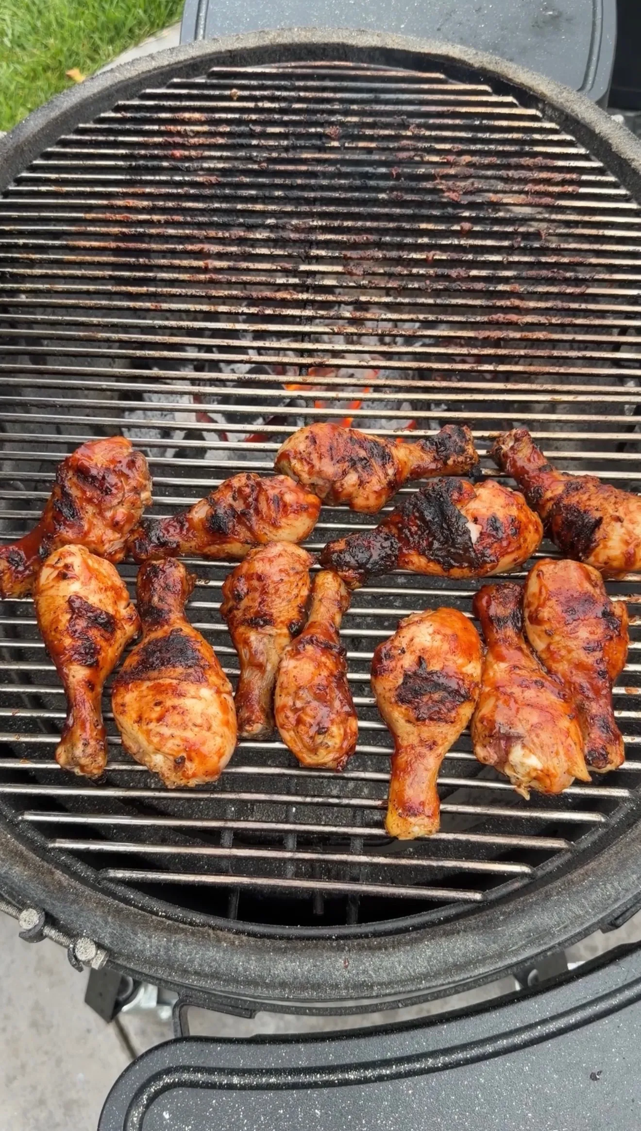 Golden brown barbecue chicken drumsticks cooking on a round charcoal grill