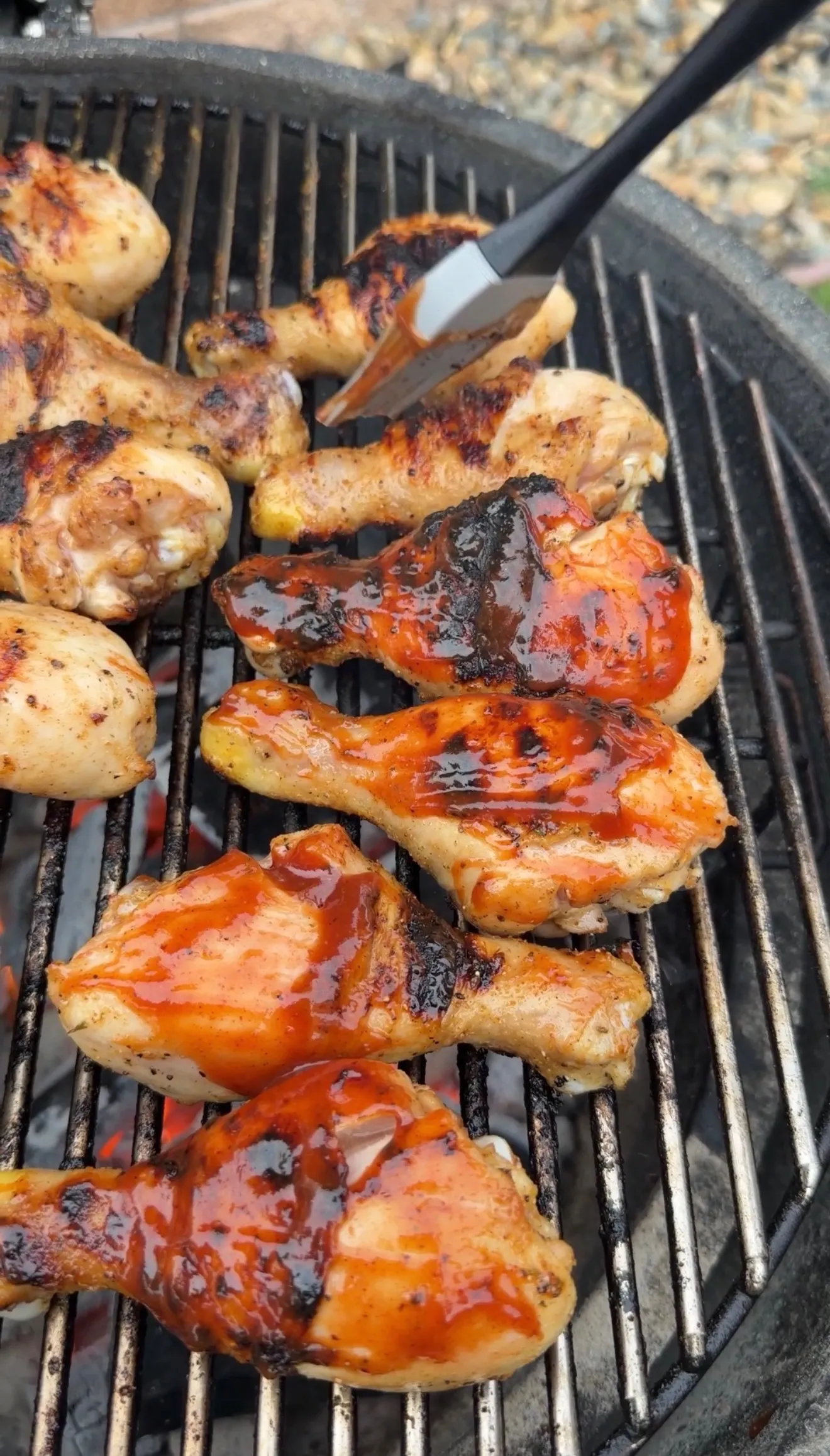 Golden barbecue chicken drumsticks on grill grates with tongs flipping glazed meat