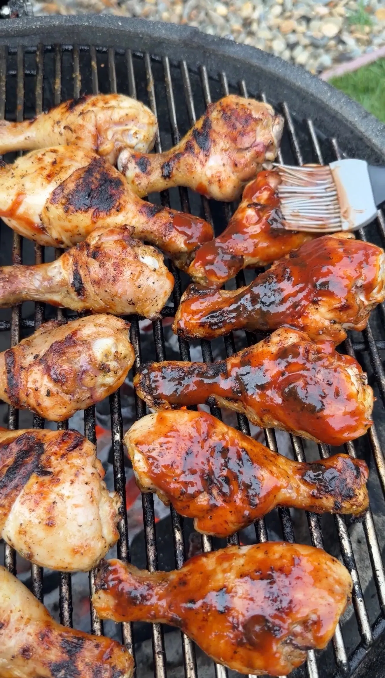 Grilled barbecue chicken drumsticks with glossy BBQ sauce on grill grates with basting brush