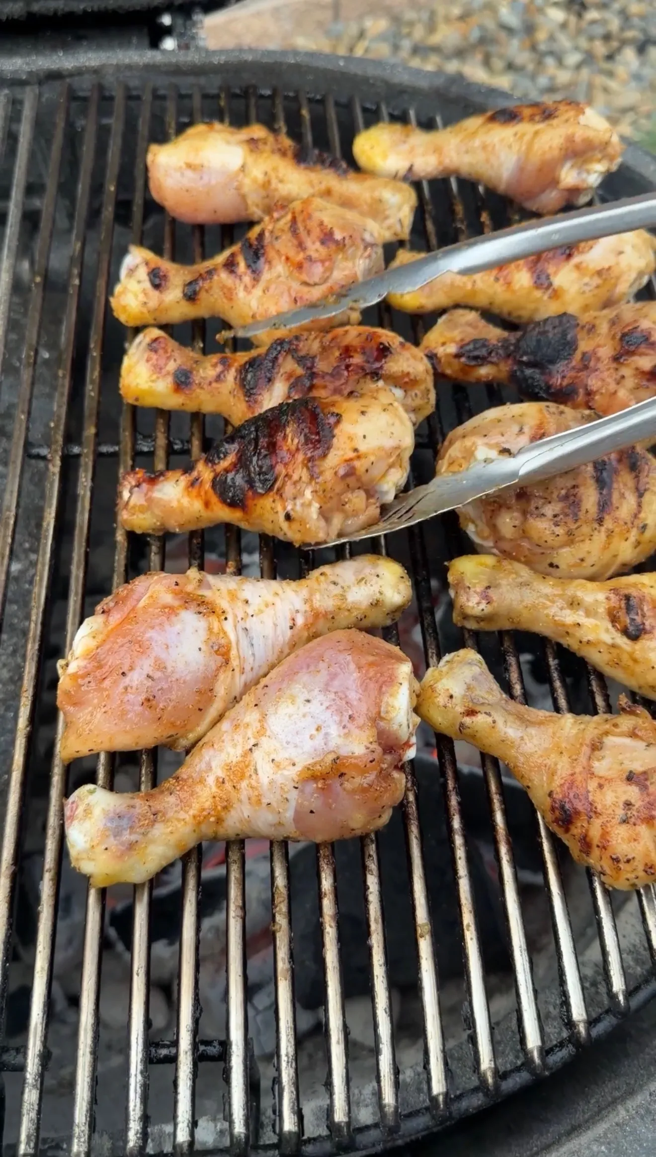 Golden-brown barbecue chicken drumsticks cooking on outdoor grill grates with tongs lifting one piece