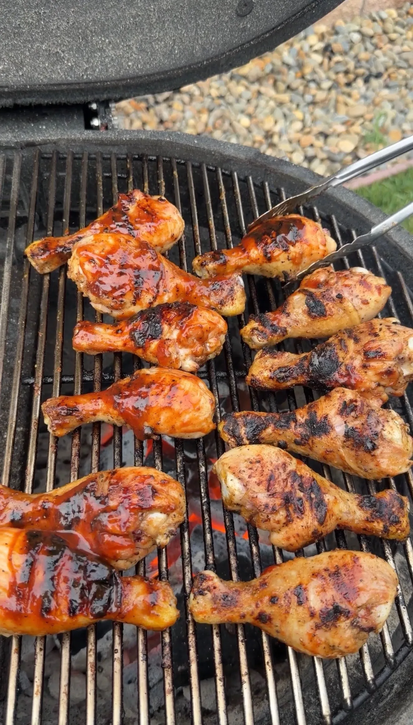 Golden brown barbecue chicken drumsticks cooking on a round grill grate with BBQ sauce glaze