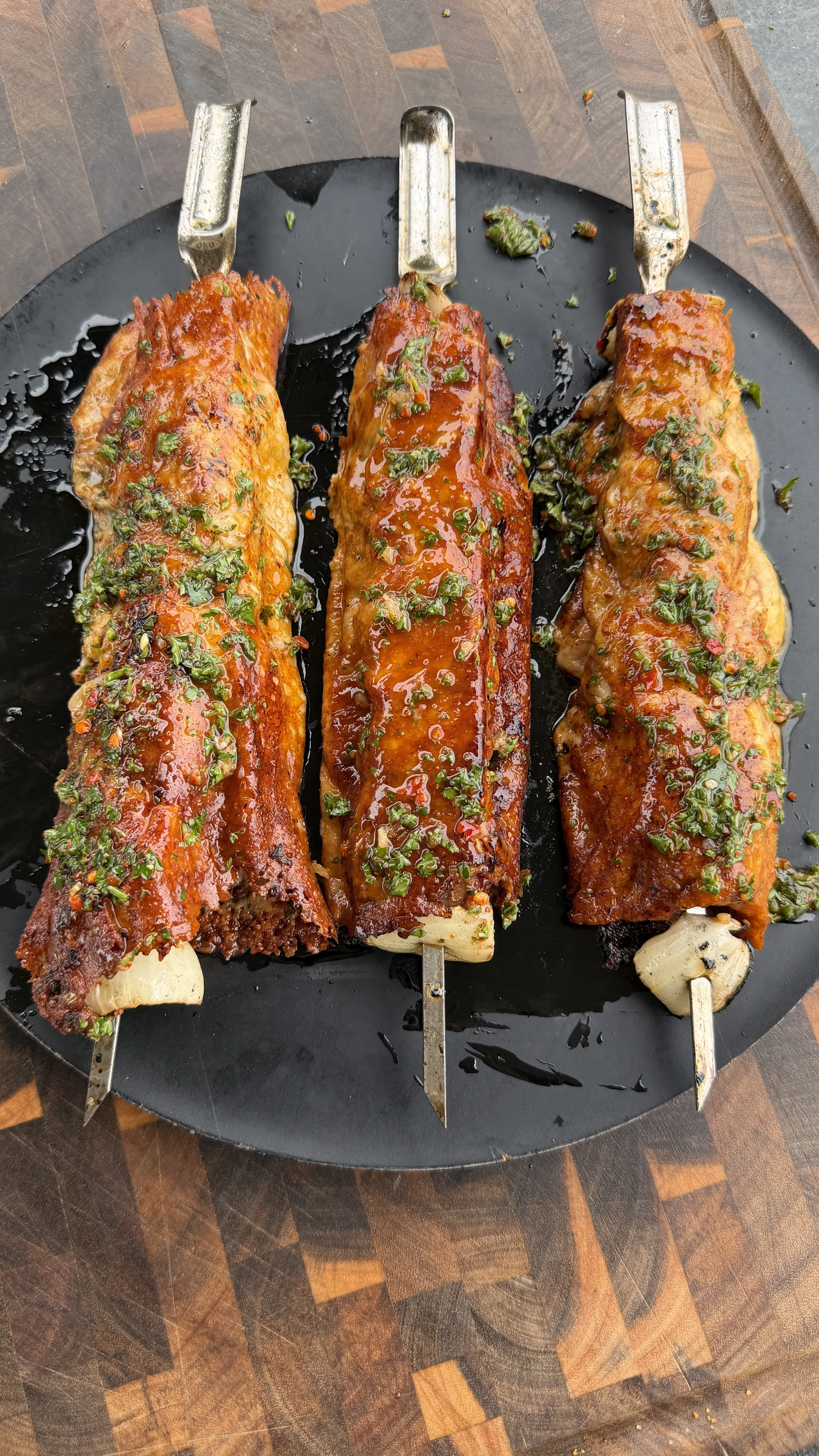 Three grilled cheese-crusted steak kebabs with chimichurri sauce on a dark round plate