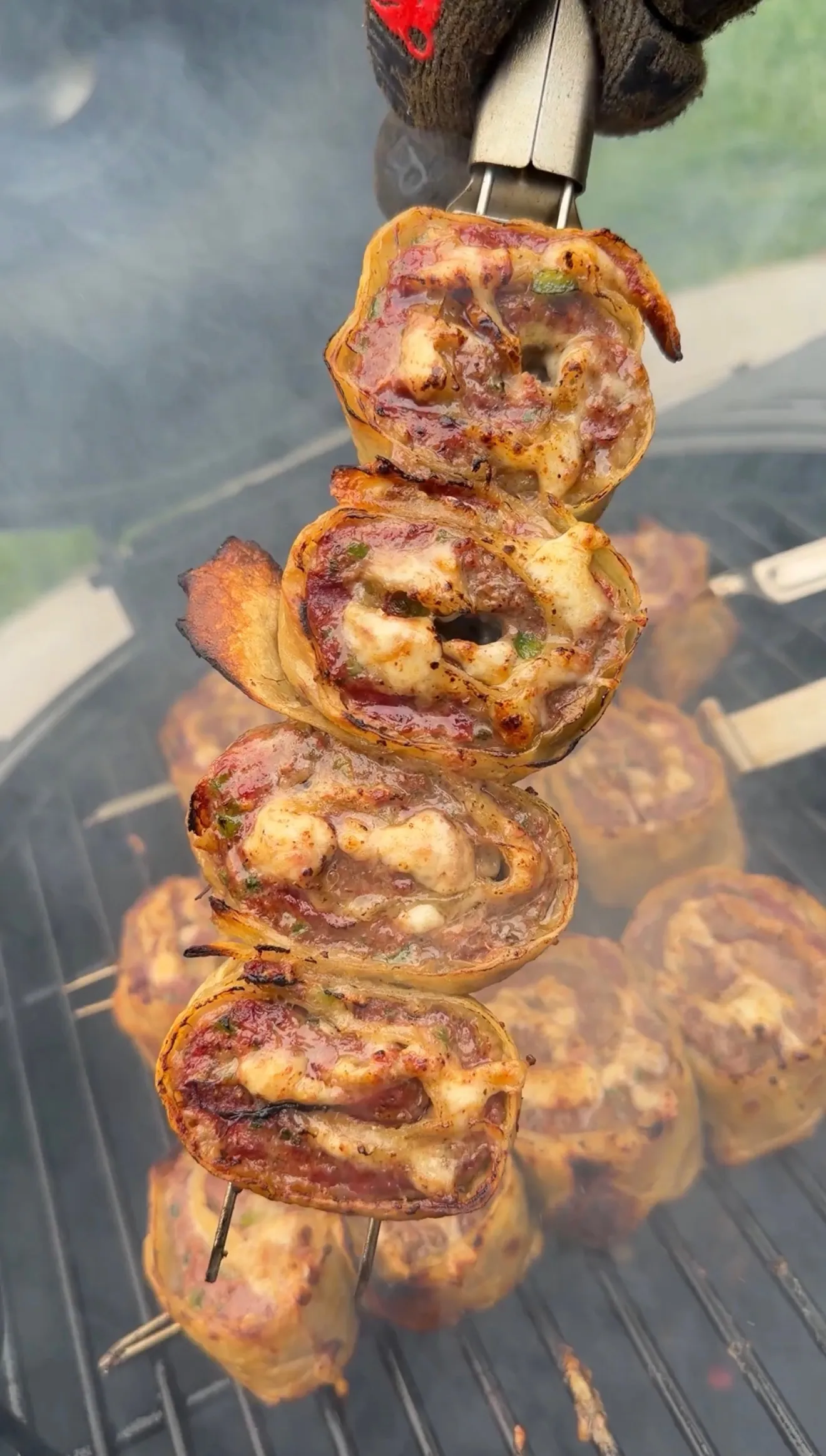 Grilled cheesy beef tortilla pinwheels threaded on a metal skewer over barbecue grill grates