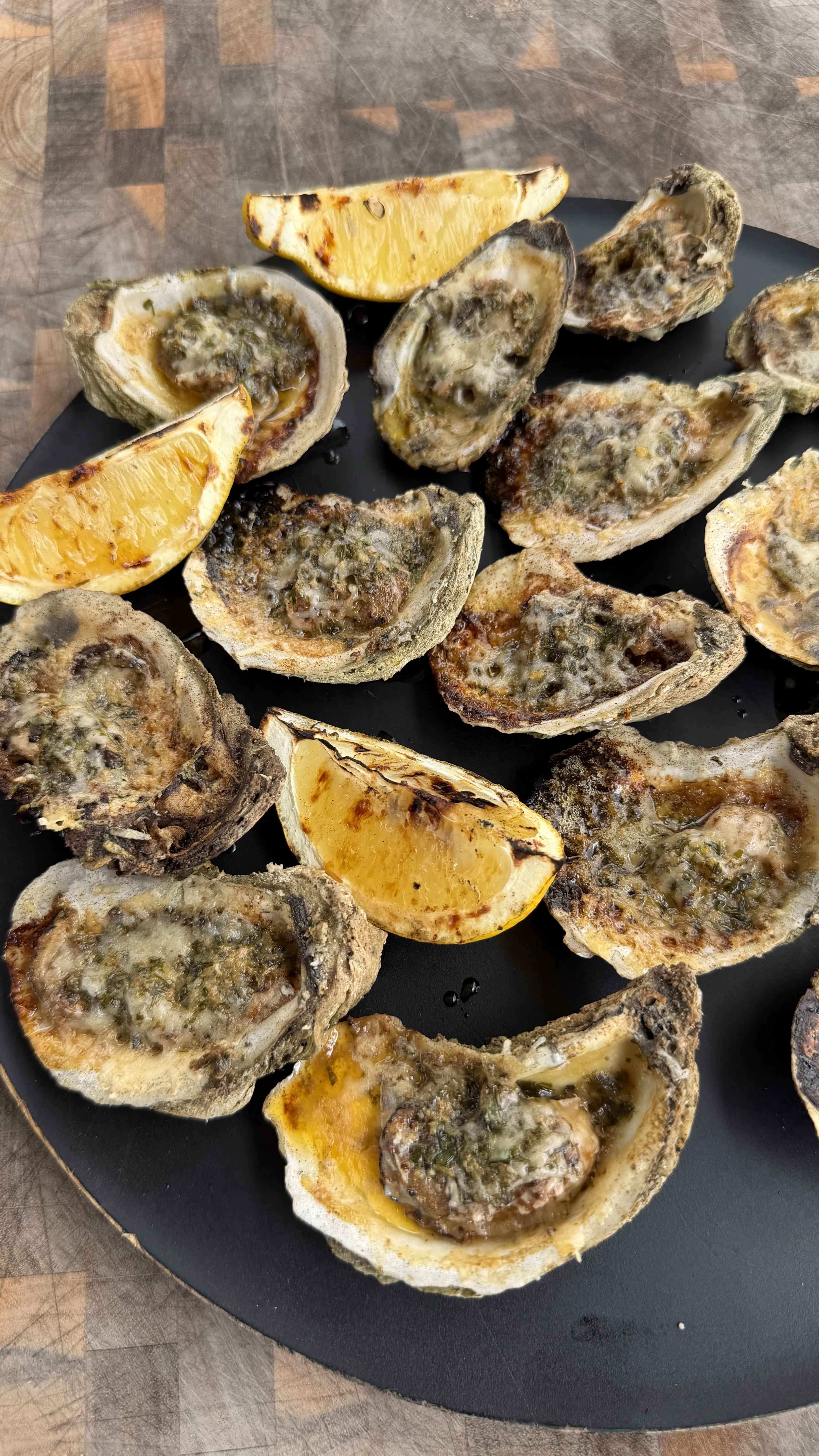 Grilled garlic herb parmesan oysters with melted cheese and herbs arranged on a slate serving plate