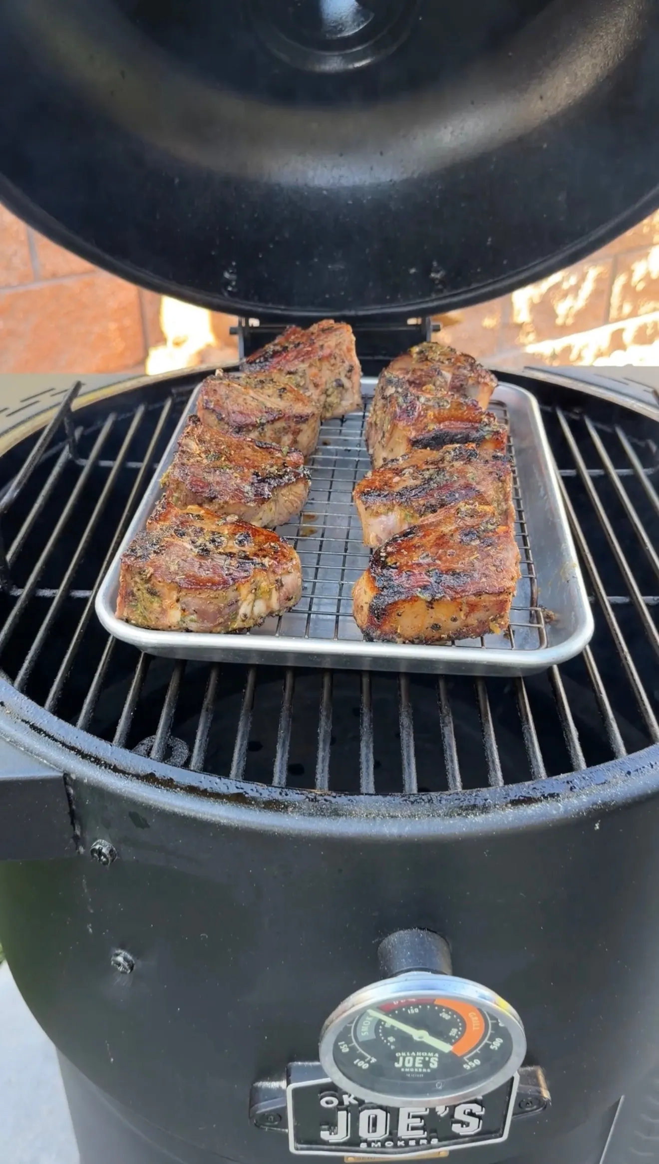 Grilled garlic herb lamb loin chops with char marks resting on cooling rack in Joe's smoker grill