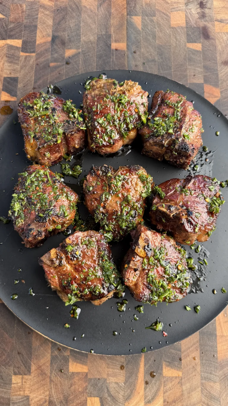 Eight grilled lamb loin chops topped with fresh green herb sauce arranged on a dark round plate