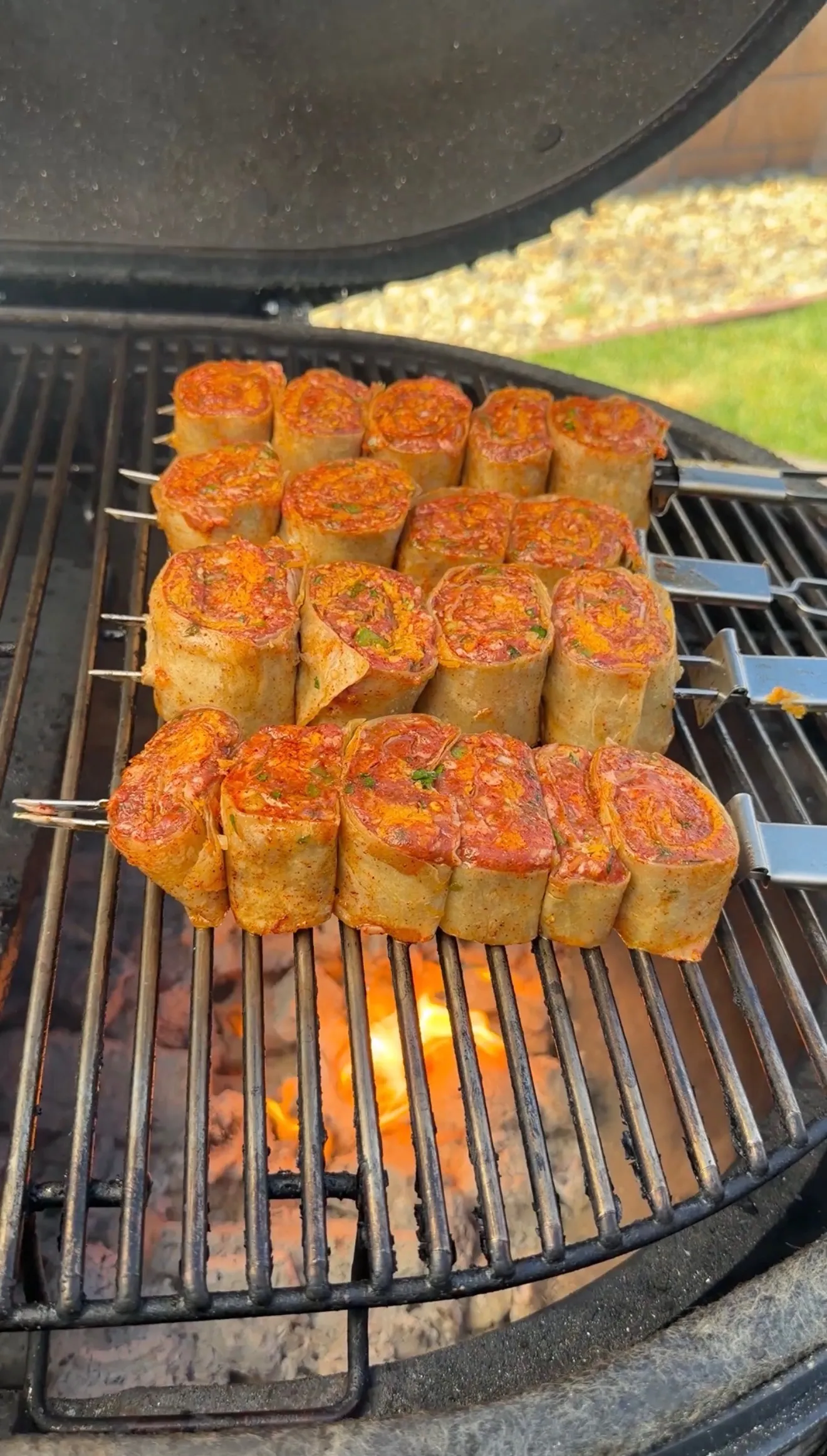 Grilled lamb tortilla pinwheel skewers cooking on barbecue grill grates with golden brown exterior