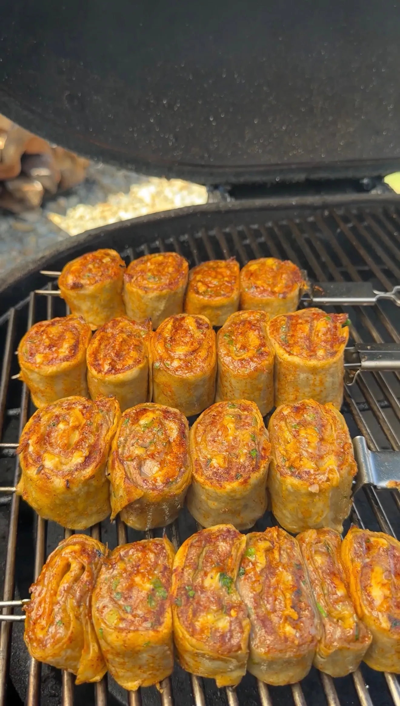 Grilled lamb tortilla pinwheel skewers cooking on barbecue grill grates with golden brown spiral patterns