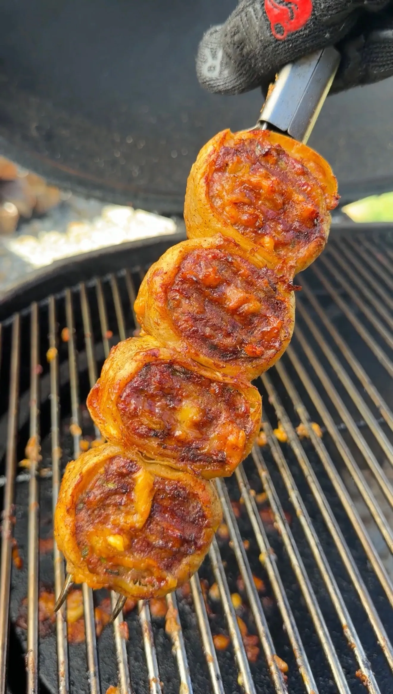 Grilled lamb tortilla pinwheel skewers with golden-brown edges cooking on a barbecue grill