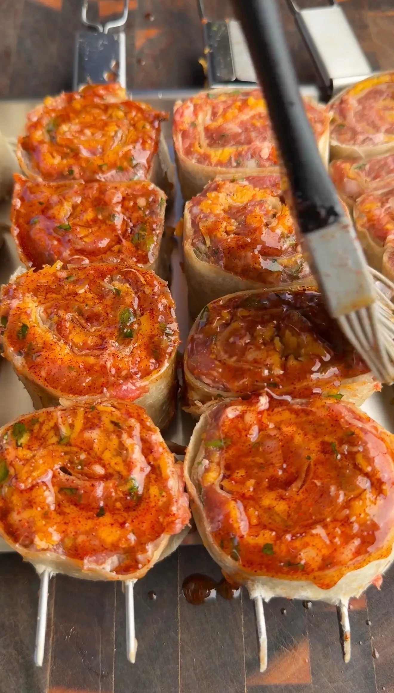 Grilled lamb tortilla pinwheel skewers with red seasoning cooking on metal grill grates