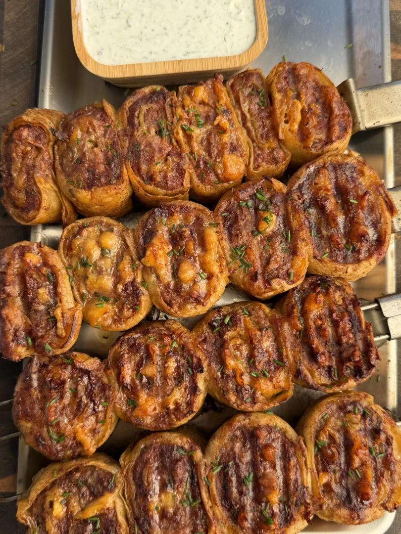Golden brown grilled lamb tortilla pinwheel skewers arranged on metal tray with herb yogurt dipping sauce