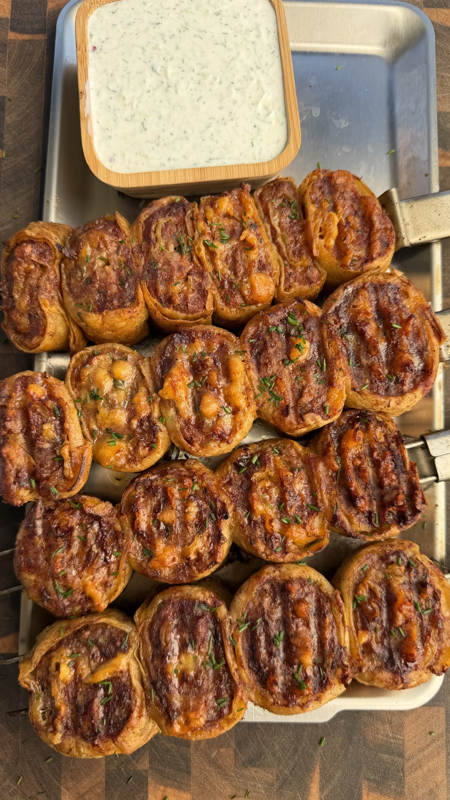 Golden brown grilled lamb tortilla pinwheel skewers arranged on metal tray with herb yogurt dipping sauce