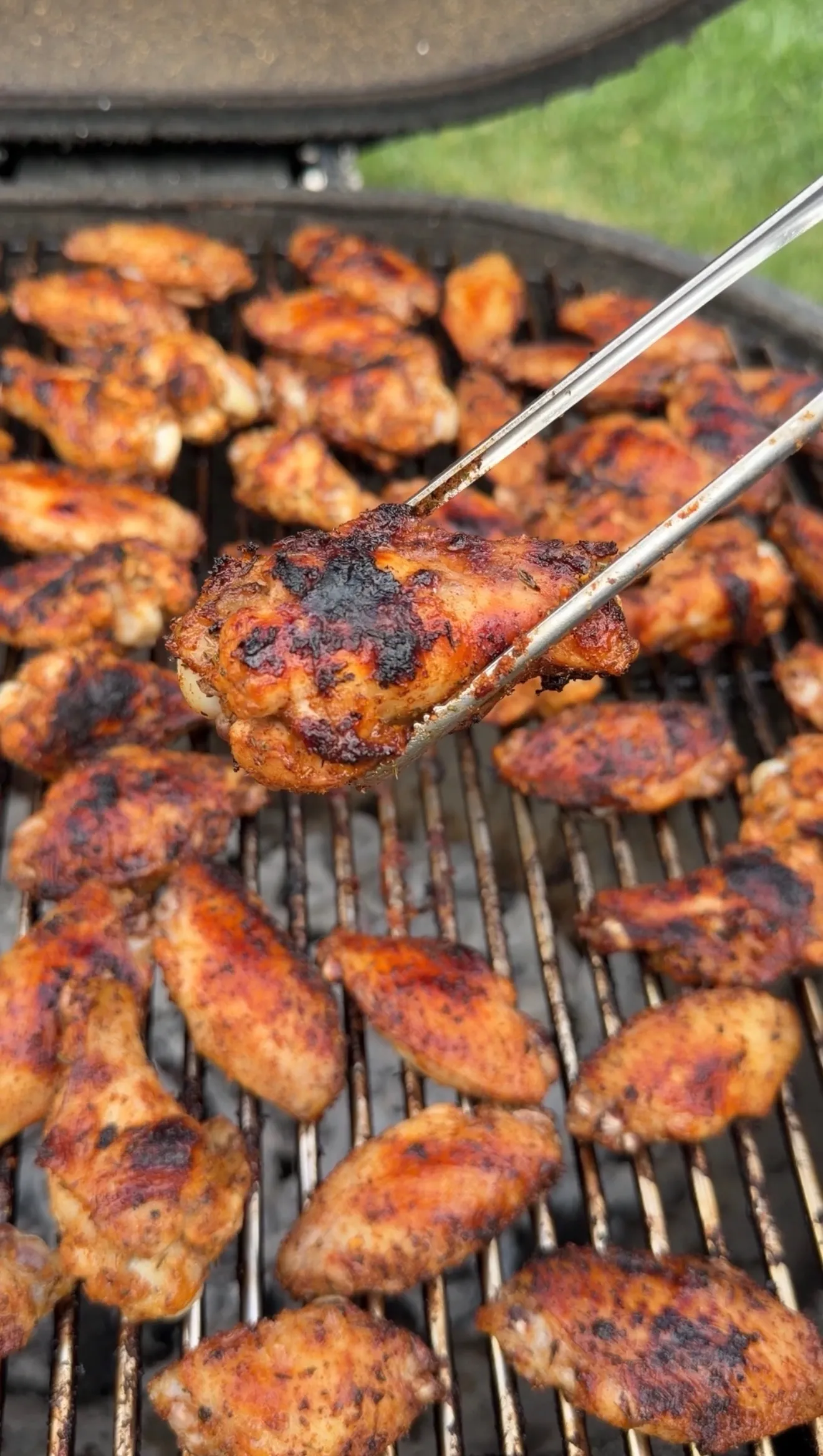 Nashville hot pickle brined chicken wings grilling on barbecue grates with tongs holding one wing