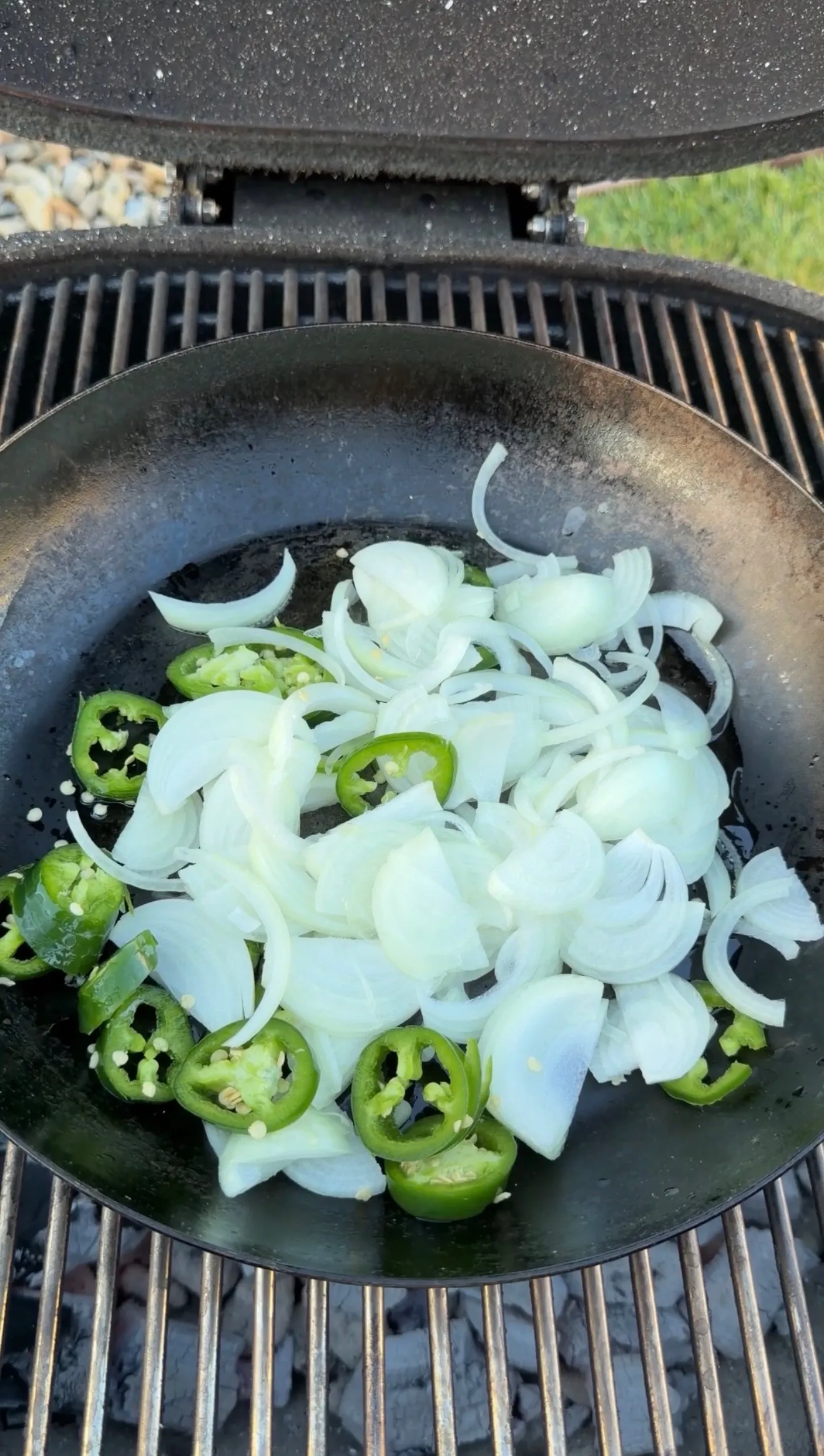 Sliced onions and jalapenos cooking in a cast iron pan on a grill for sausage stuffed bread boats