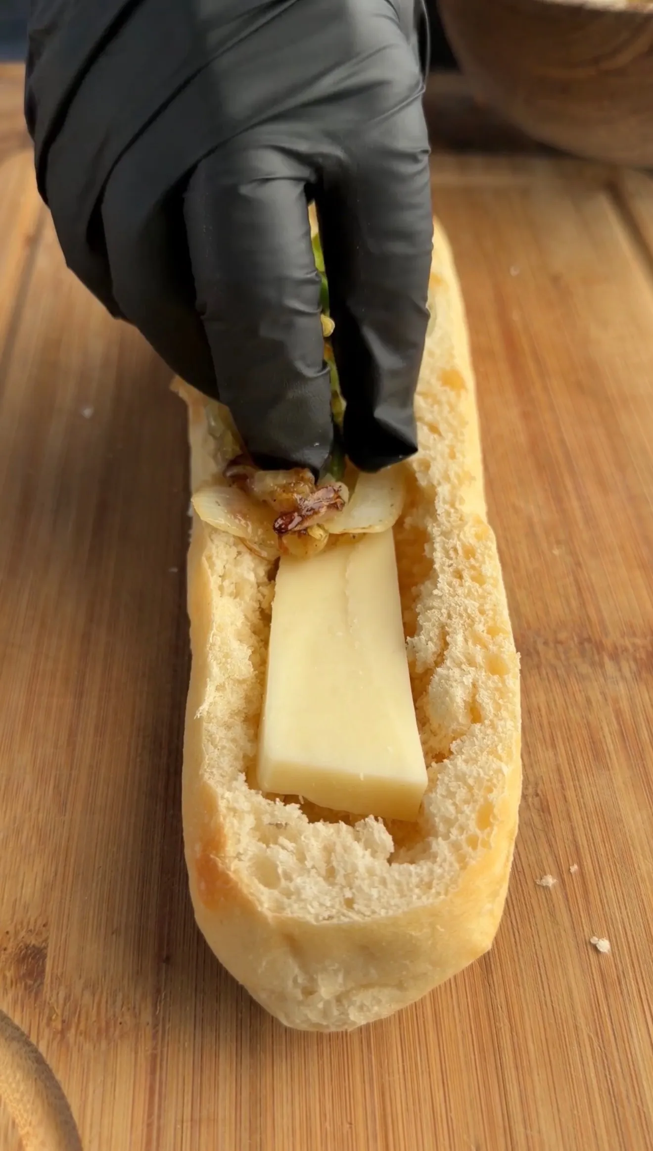 Hands in black gloves placing cheese into hollowed bread boat for grilled sausage stuffed bread recipe