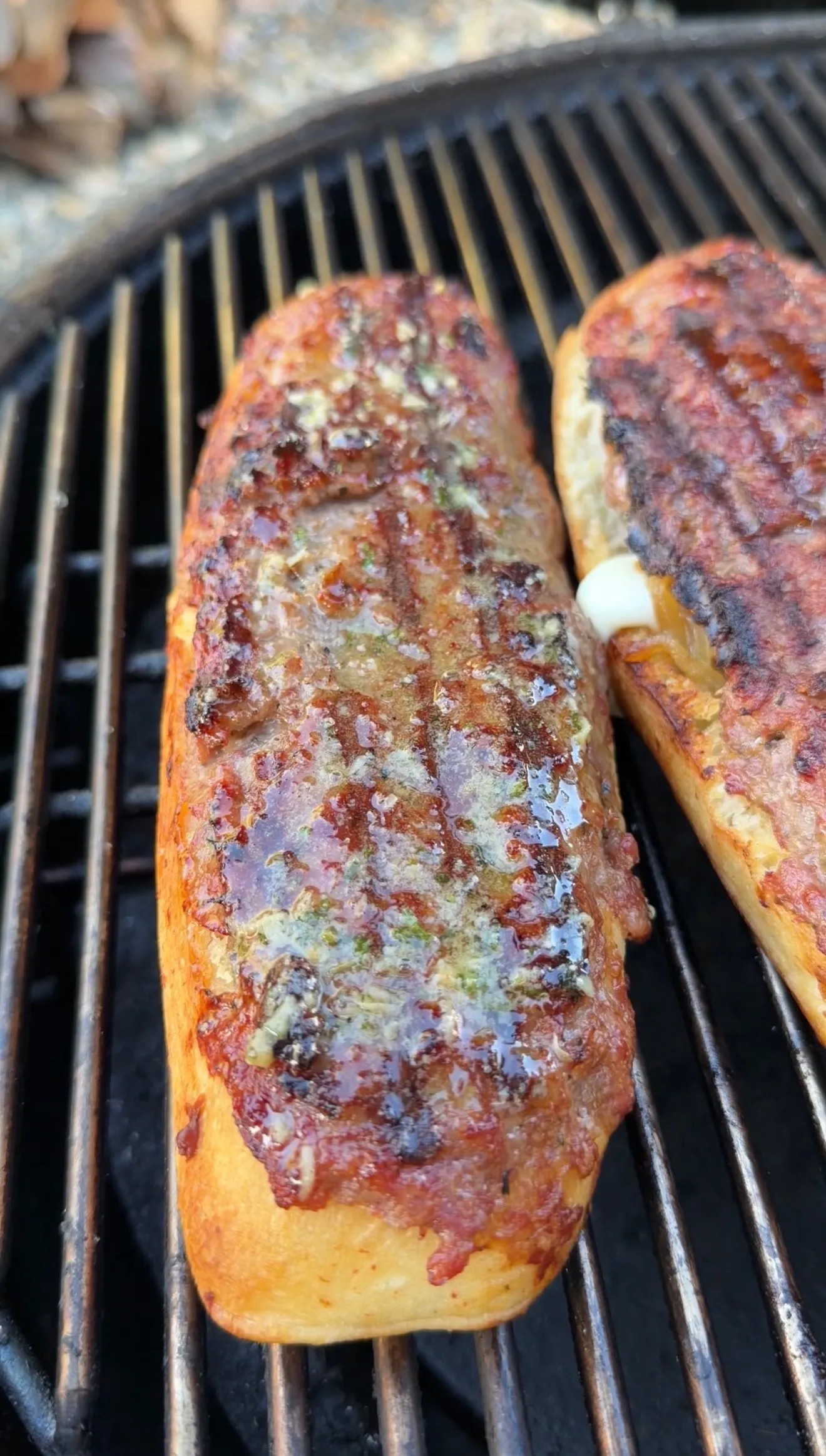Two grilled sausage stuffed bread boats with melted cheese and herbs cooking on barbecue grill grates