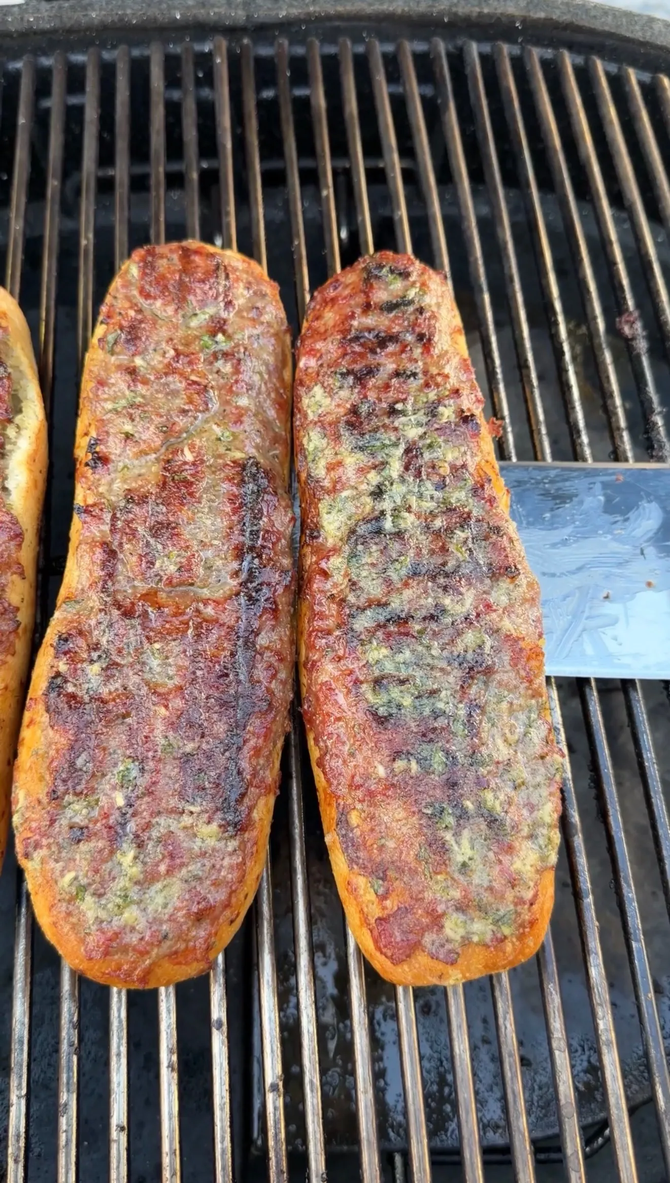 Two grilled sausage stuffed bread boats cooking on barbecue grill grates
