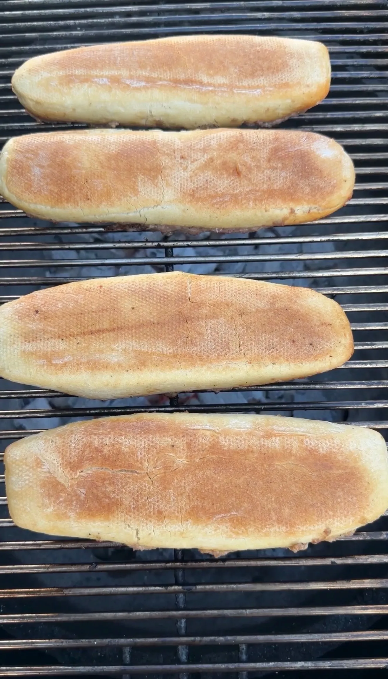 Four golden-brown sausage stuffed bread boats cooking on a metal grill grate