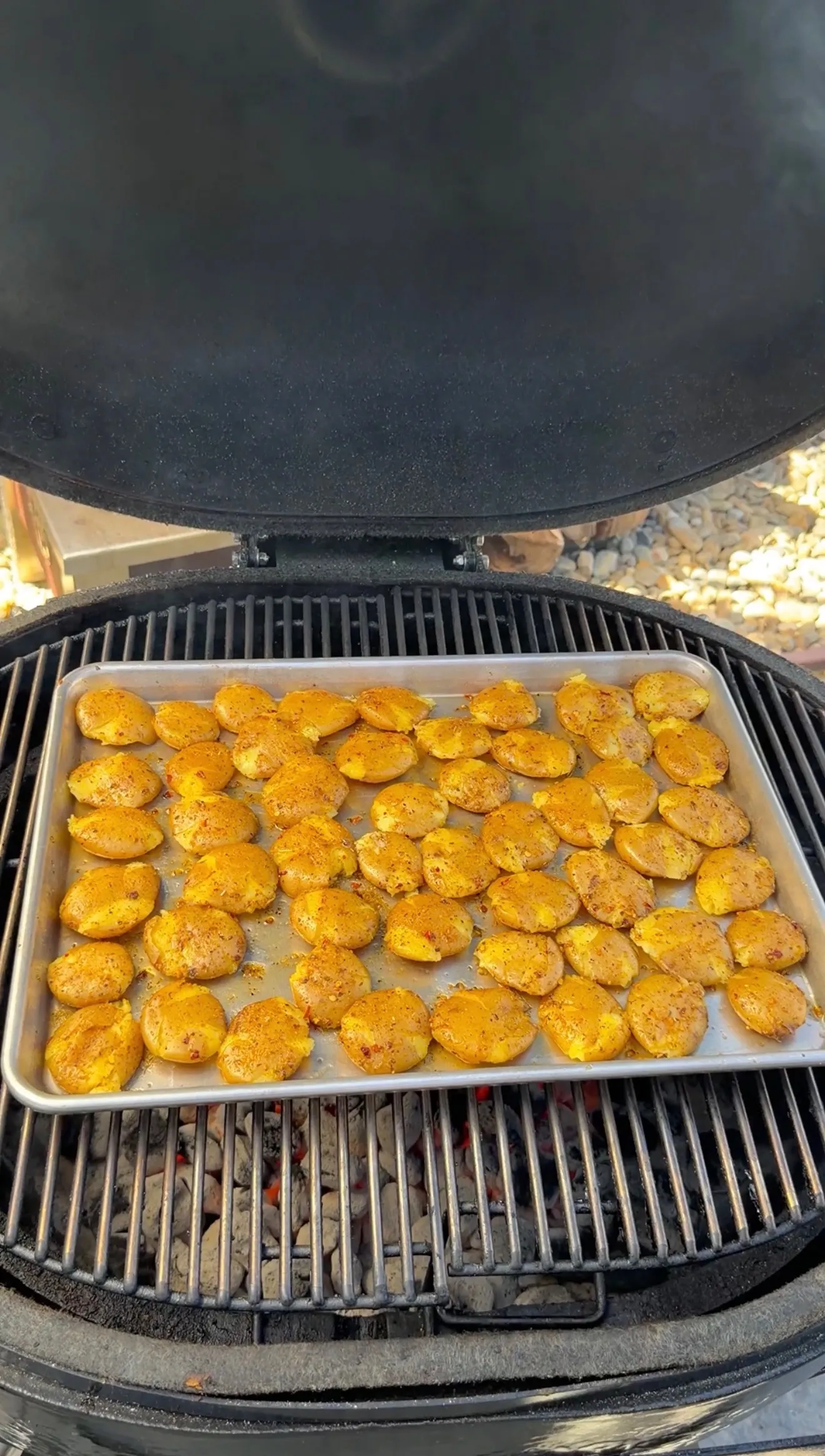 Golden smashed mini potatoes seasoned with spices cooking on a baking sheet on a round grill