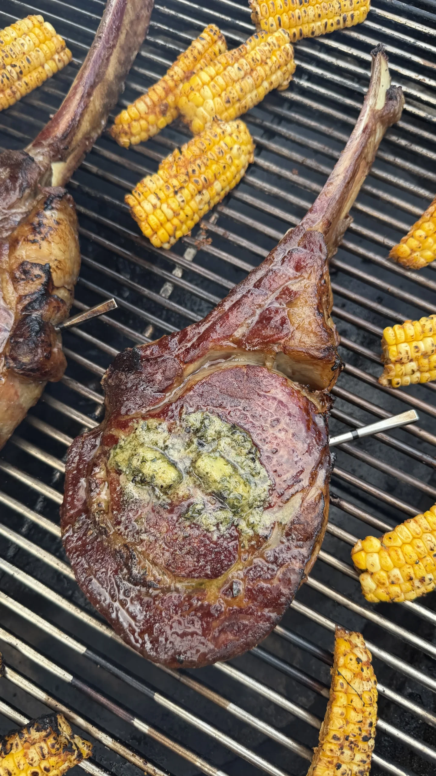 Grilled tomahawk steak with herb butter alongside charred mini corn ribs on barbecue grill grates