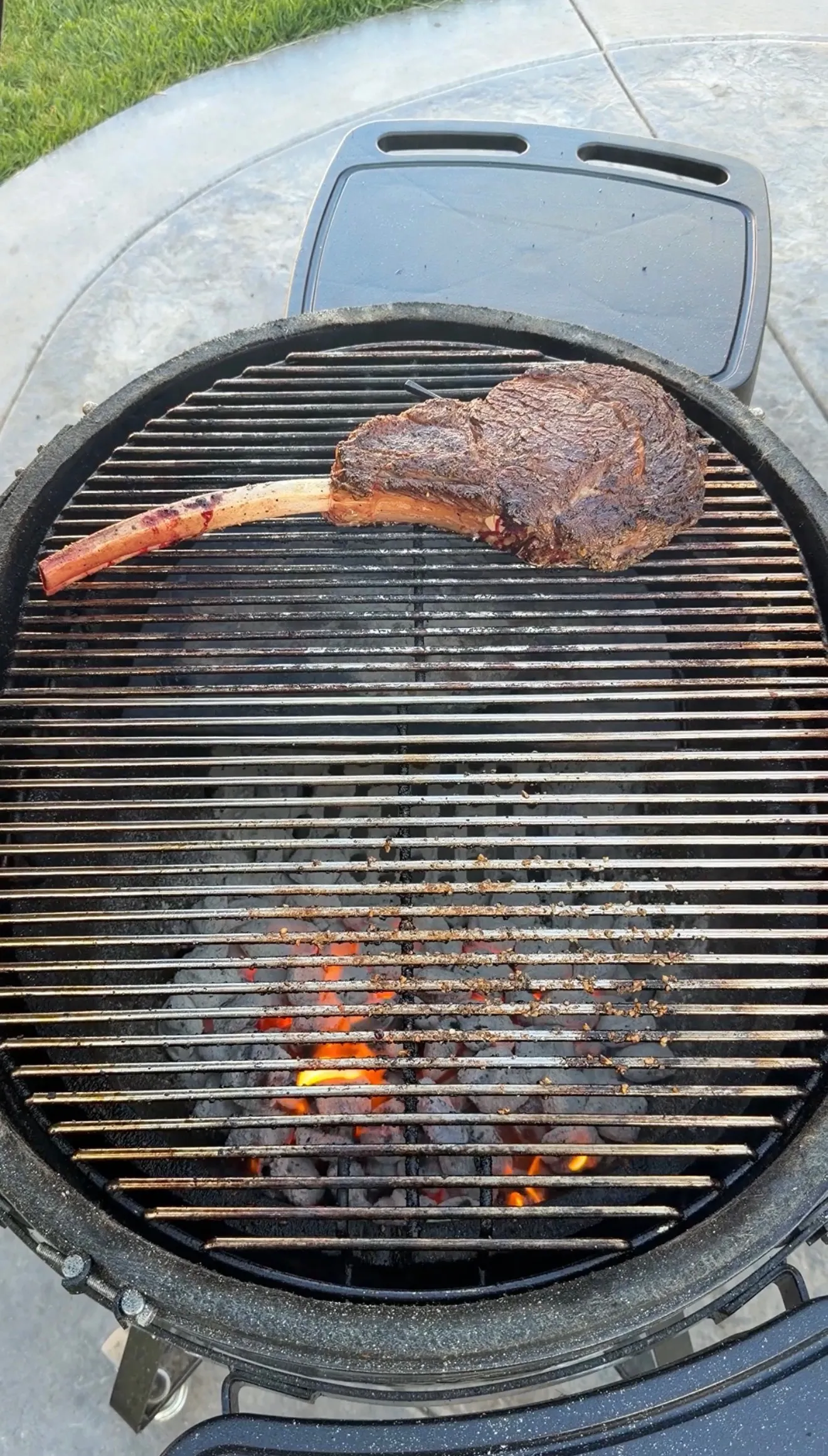 Large tomahawk steak with long bone grilling on charcoal grill grates with visible flames underneath