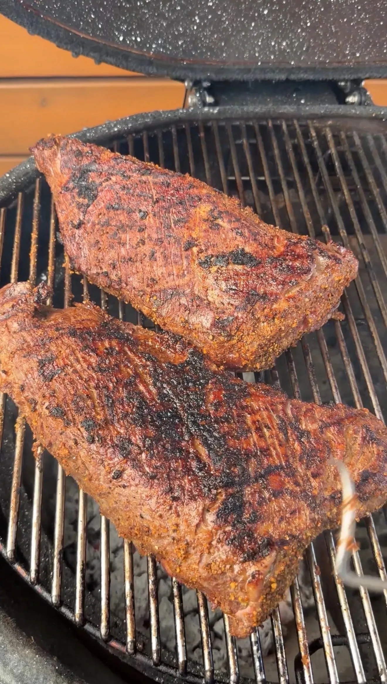 Seasoned tri-tip roast with dark charred crust cooking on barbecue grill grates